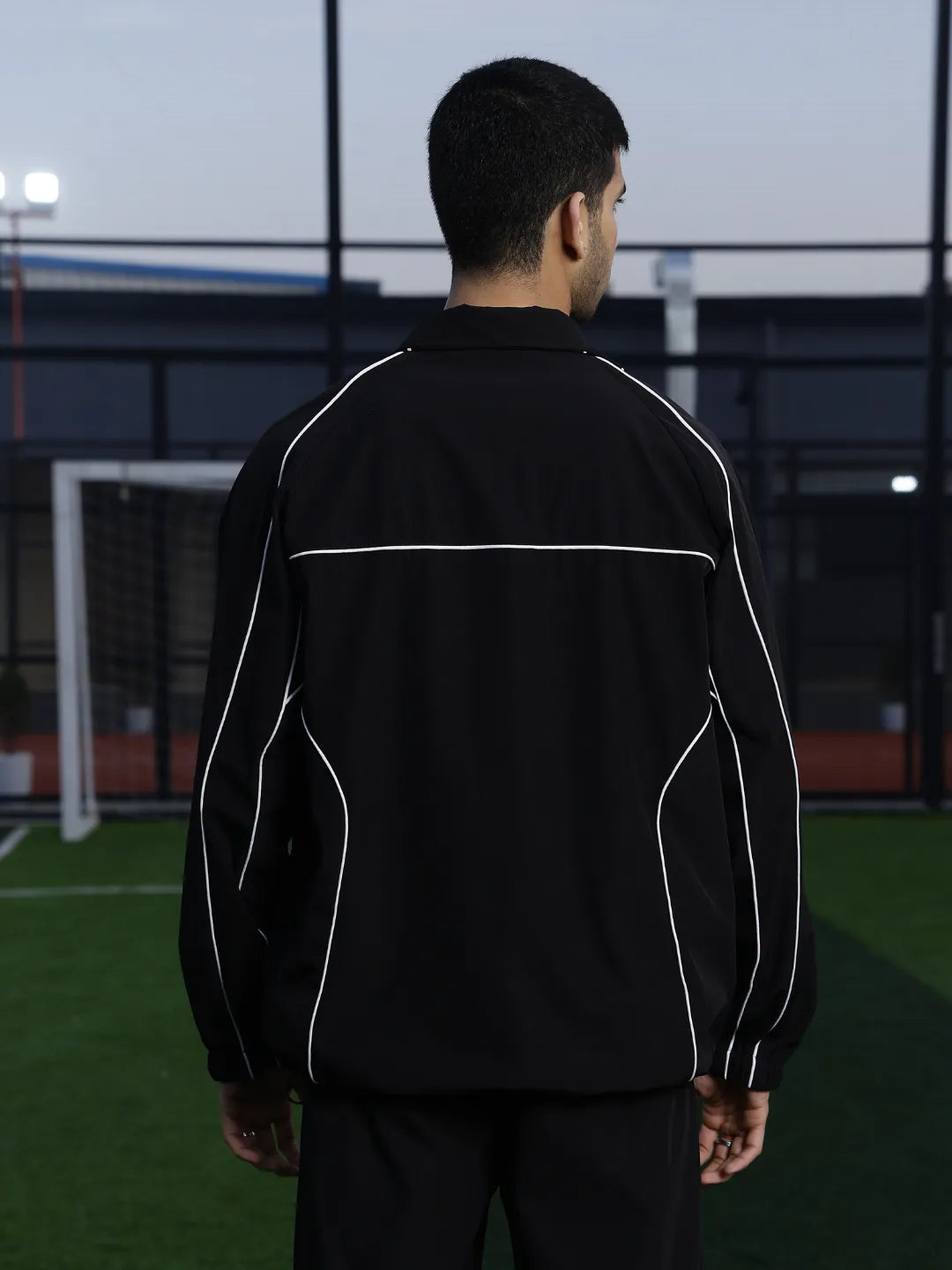 Person wearing a black sports jacket with white accents on a sports field.