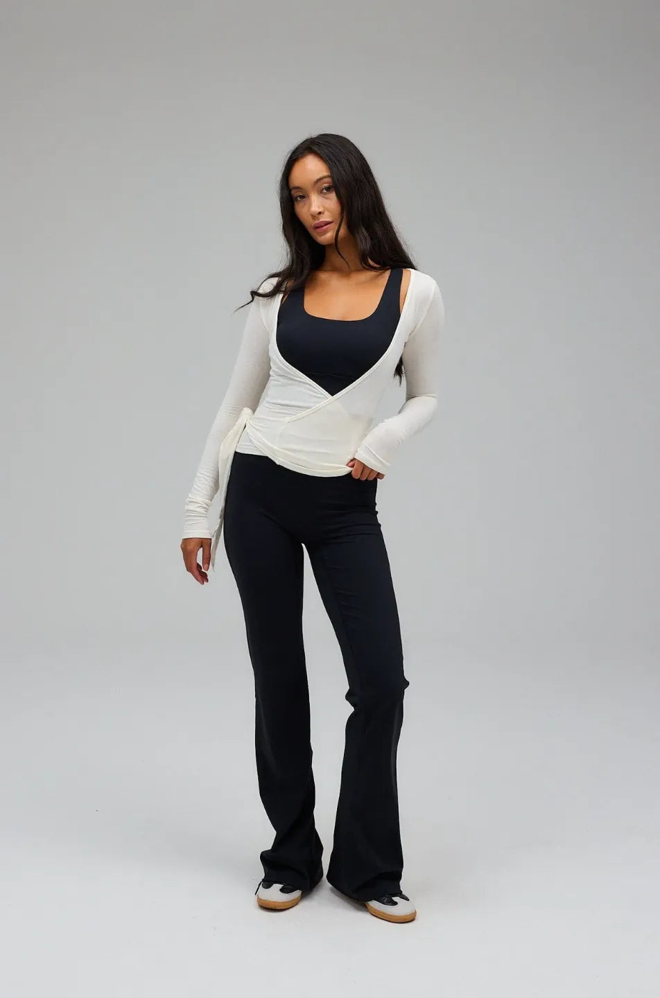 Woman wearing a white long-sleeve top and black pants on a grey background