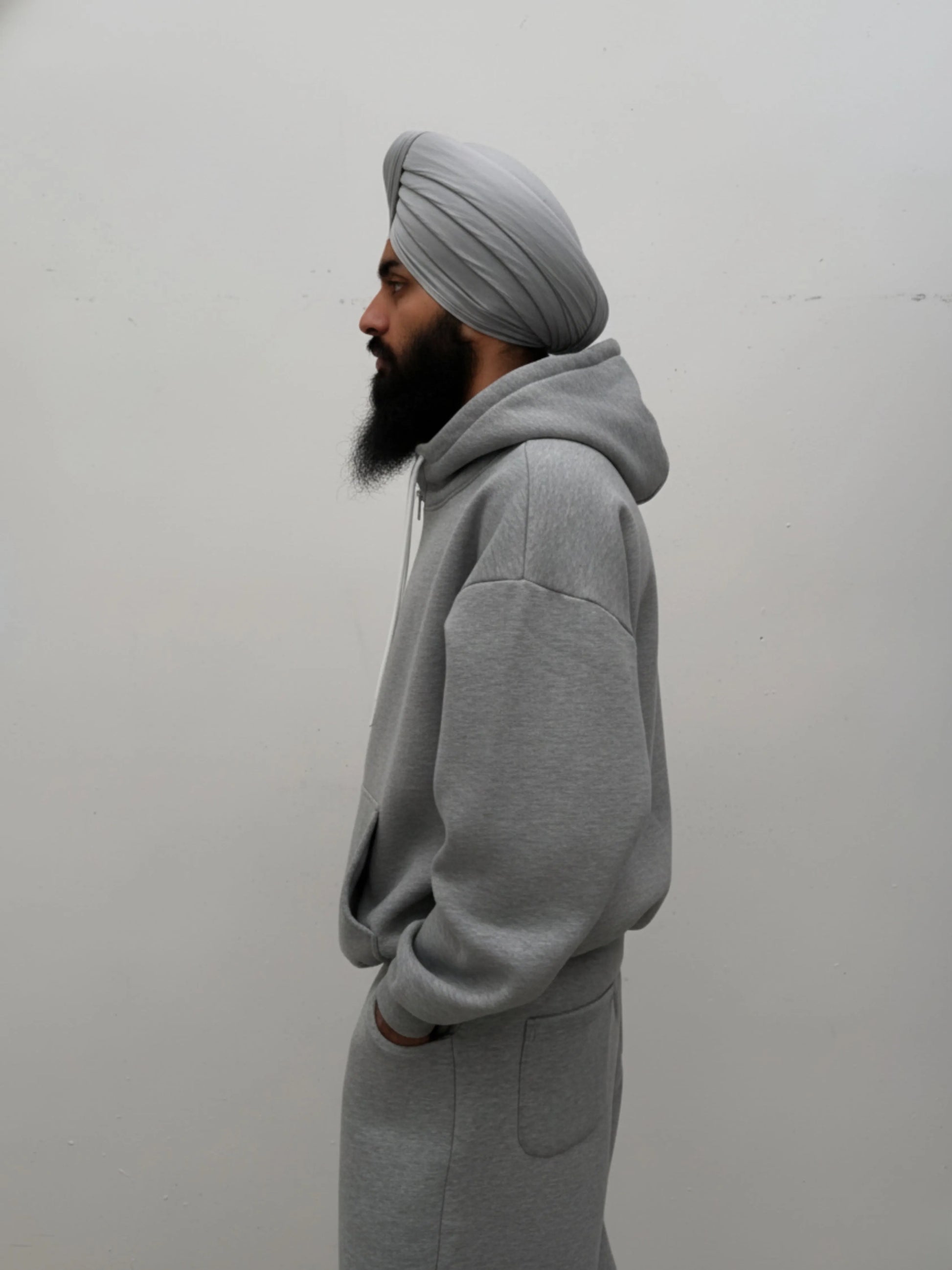 Person wearing a grey hoodie and turban against a plain background