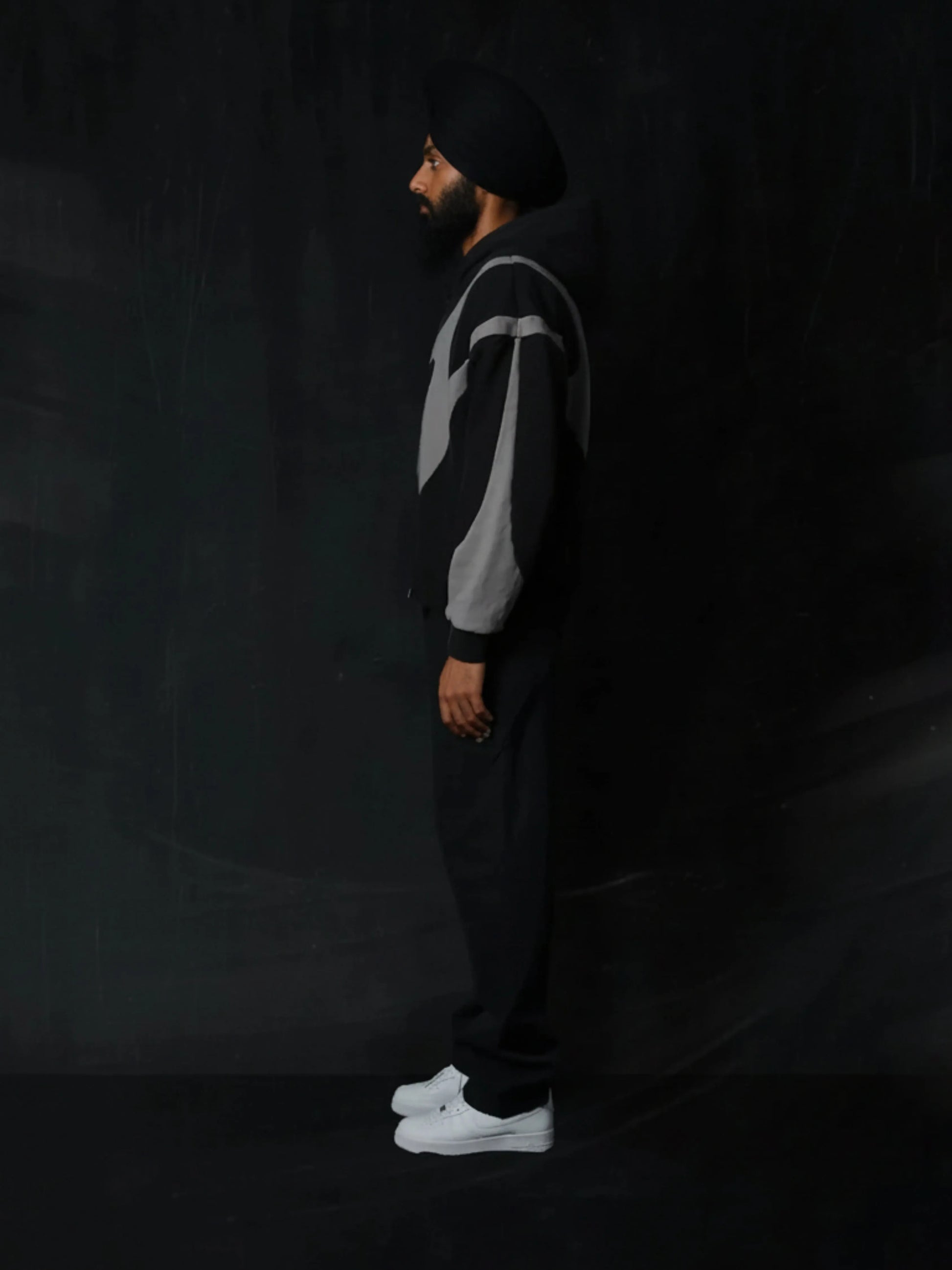 Person wearing a black and grey hoodie with white sneakers on a dark background
