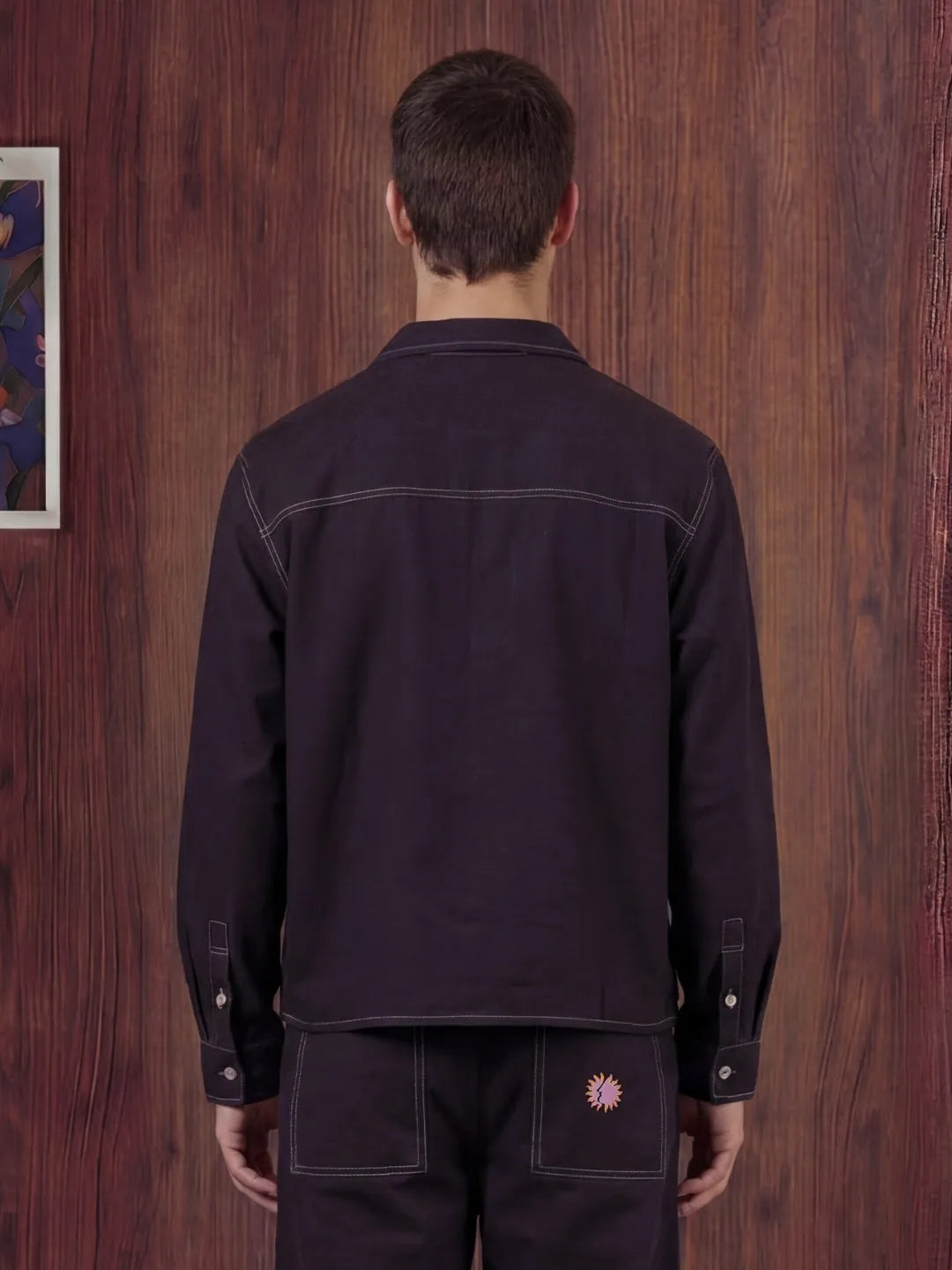 Person wearing a black shirt and pants against a wooden wall.