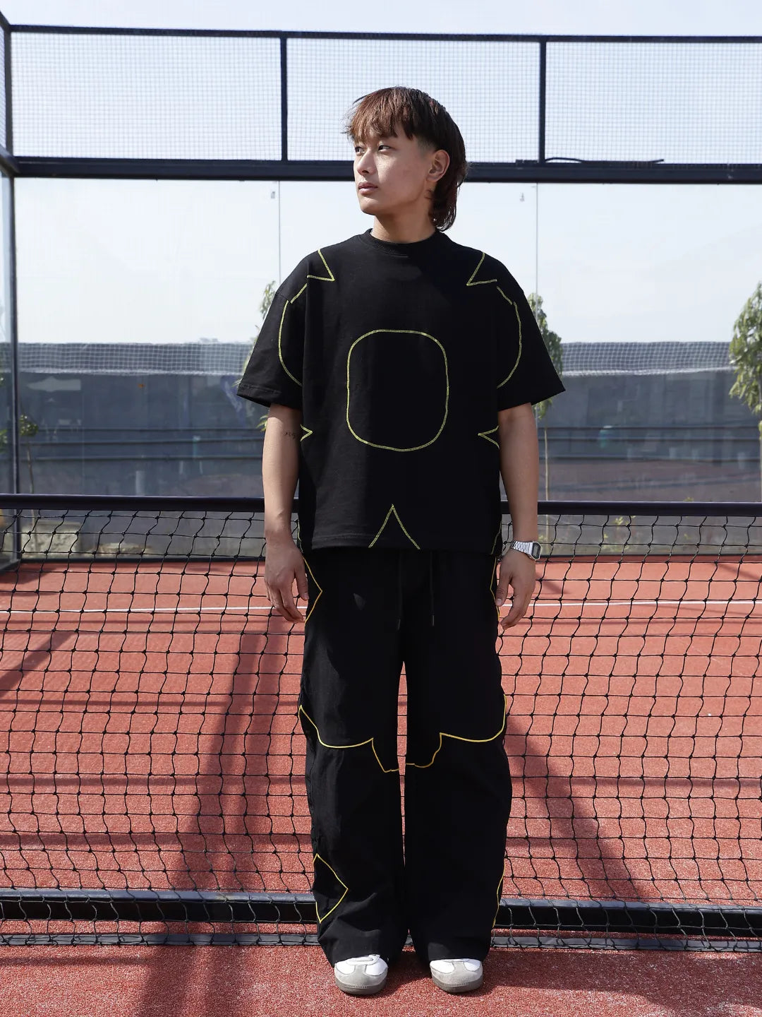 Person wearing a black outfit with yellow accents on a tennis court.