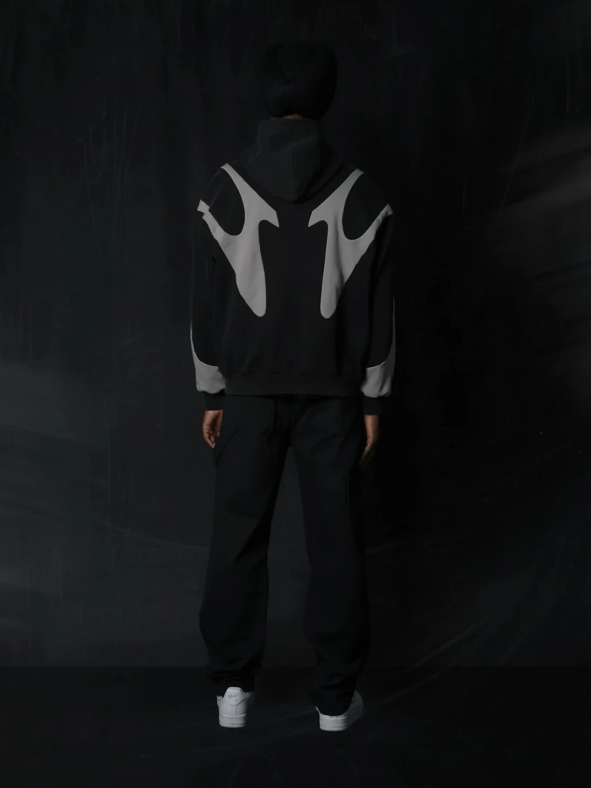 Person wearing a black hoodie with white logo on the back against a dark background