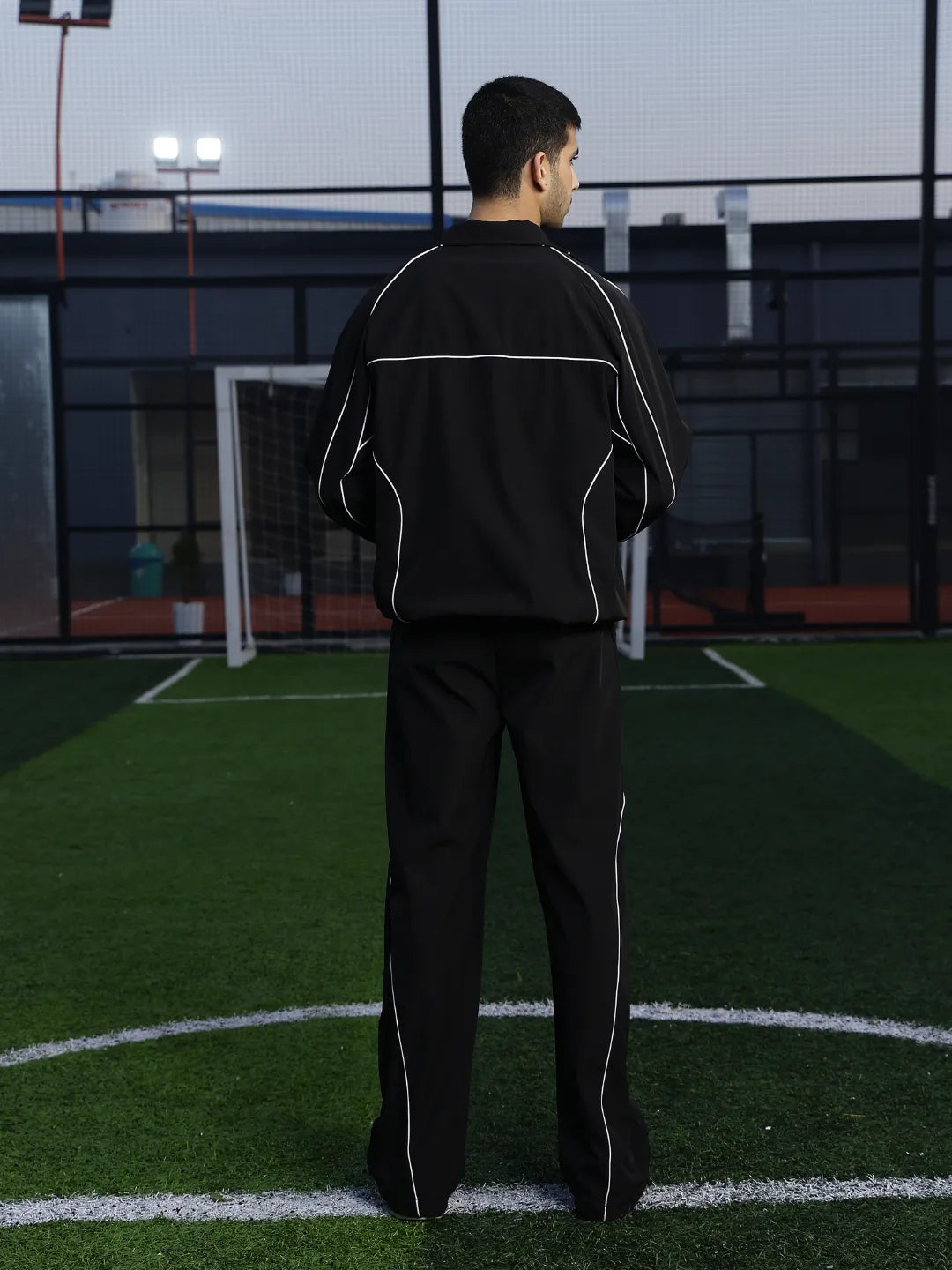 Person wearing a black tracksuit with white stripes on an outdoor sports field.