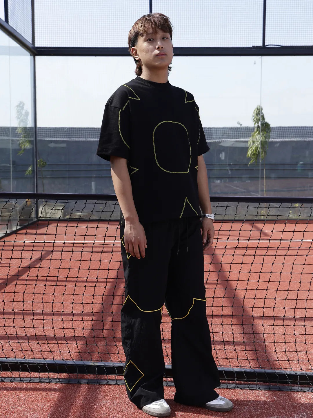 Person wearing a black outfit with yellow accents on a tennis court.