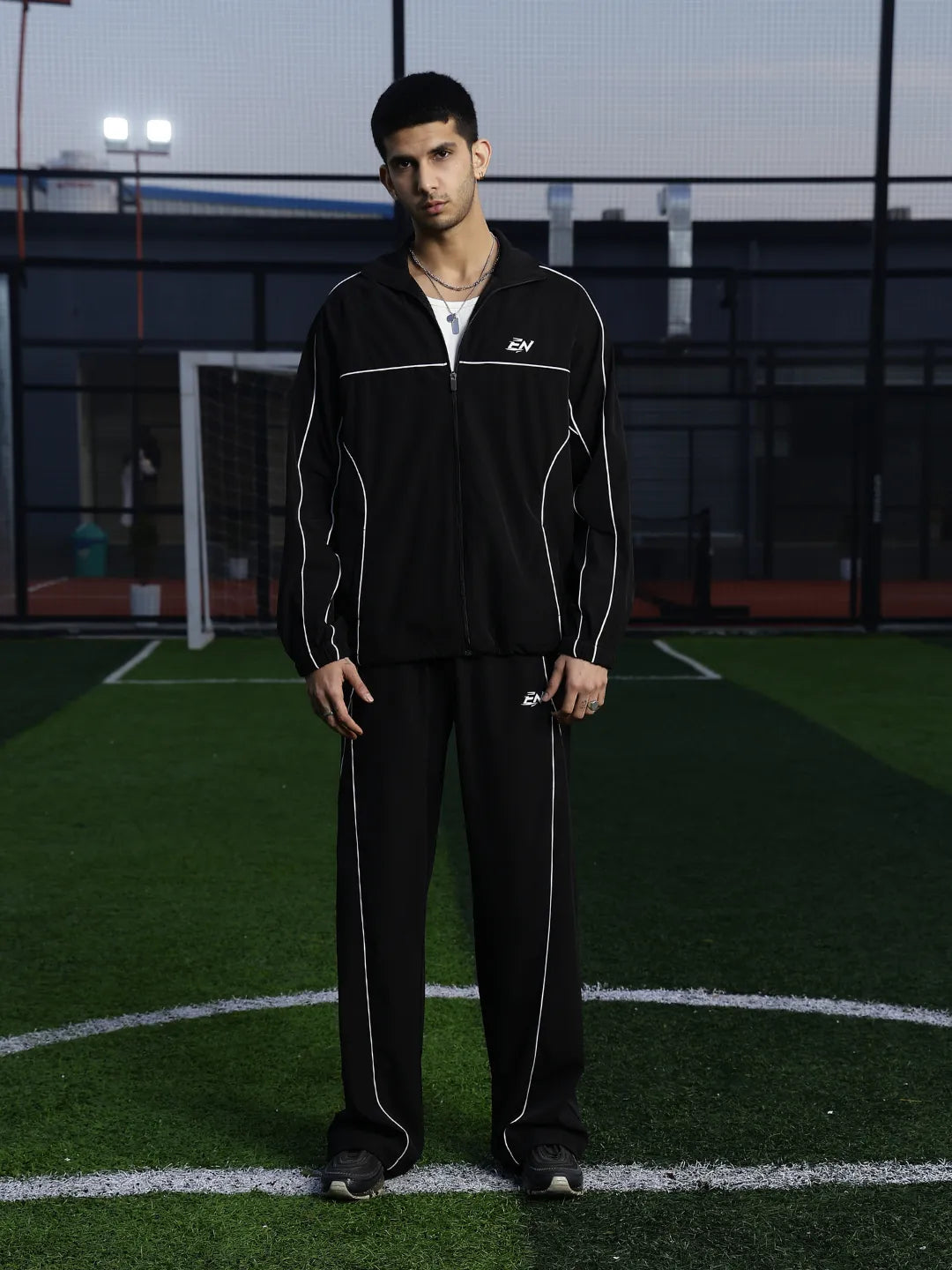 Man wearing a black tracksuit with white accents on a sports field.