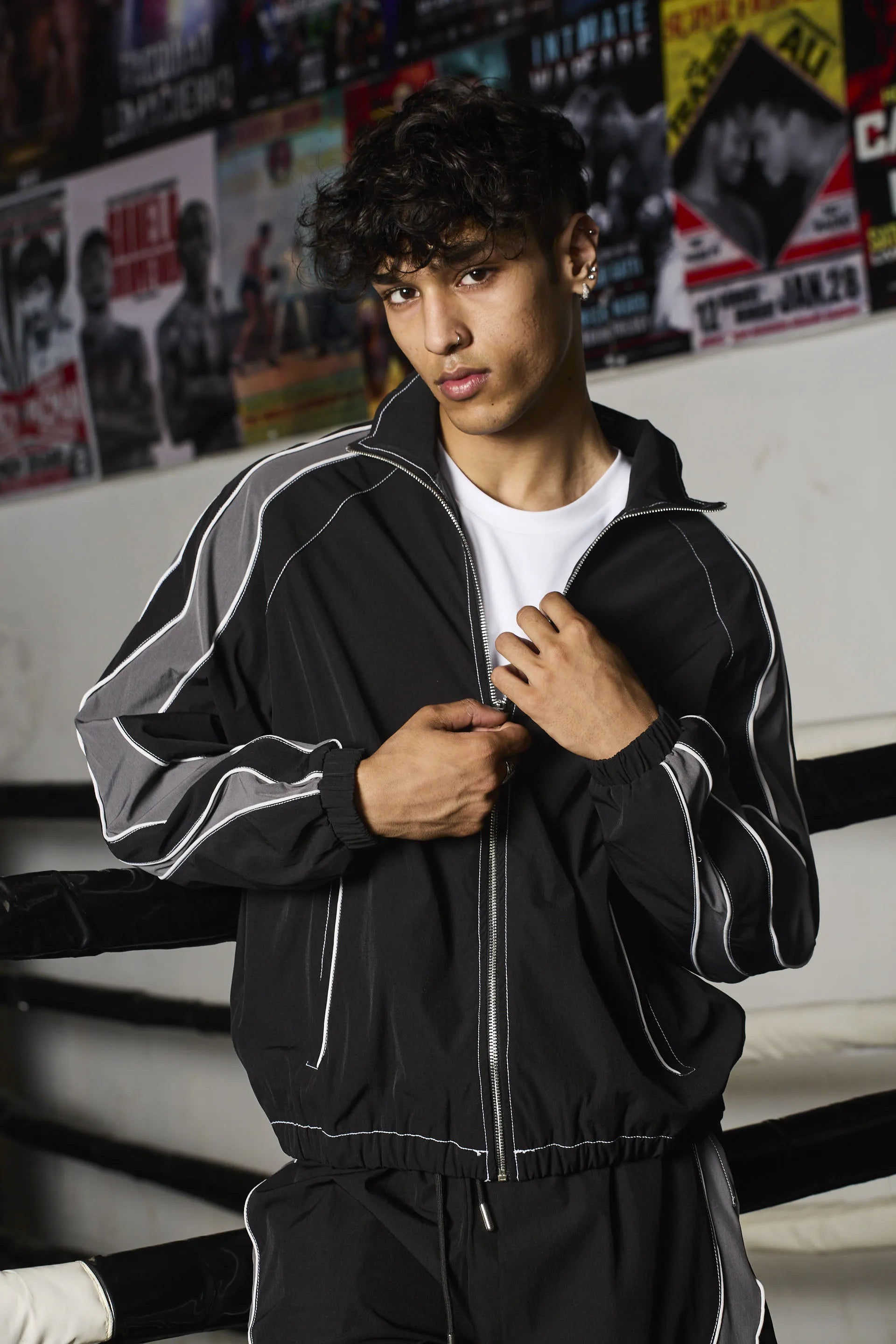 Person wearing a black tracksuit with white stripes in a boxing ring setting.