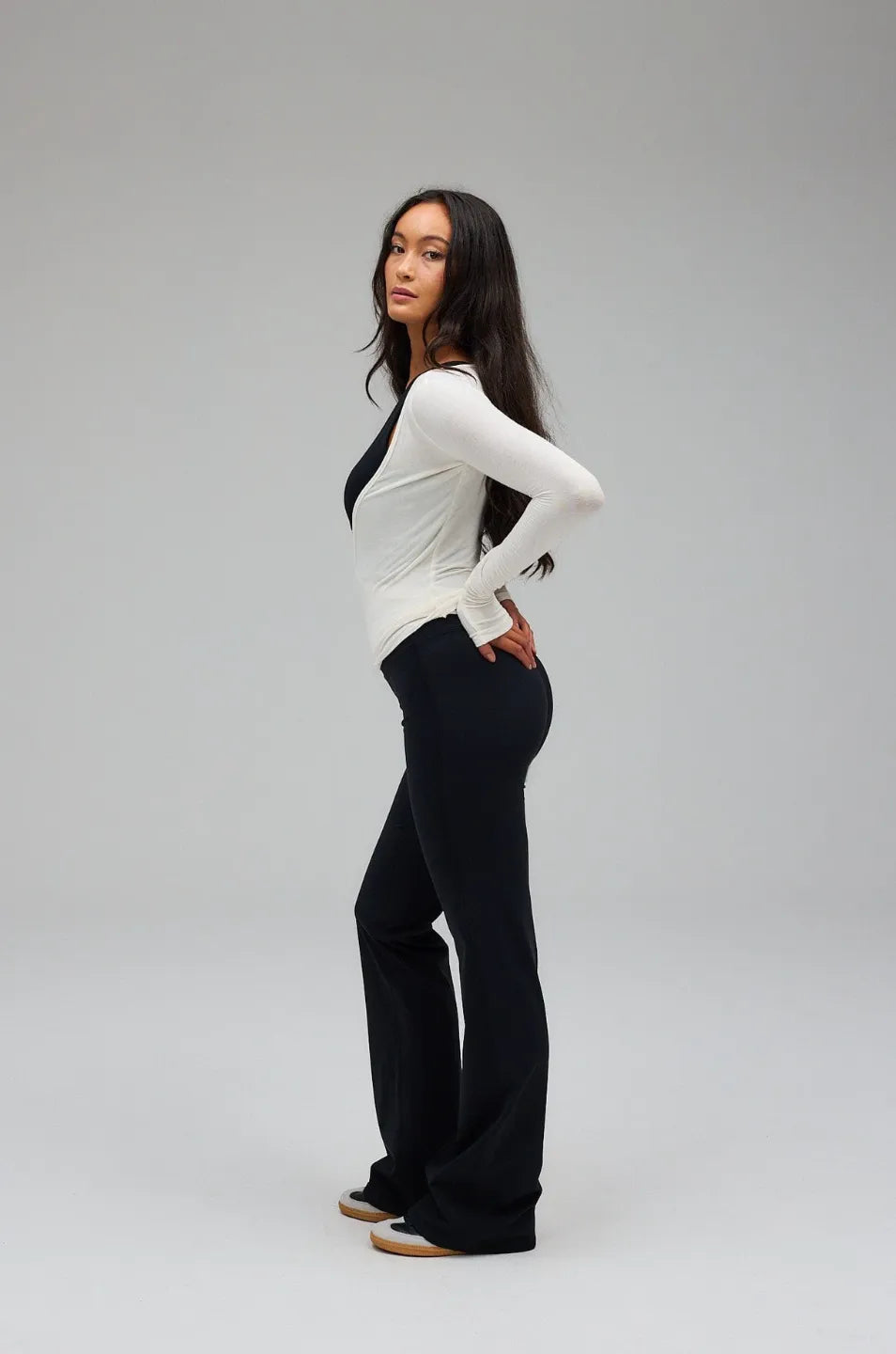 Woman wearing a white top and black pants on a grey background