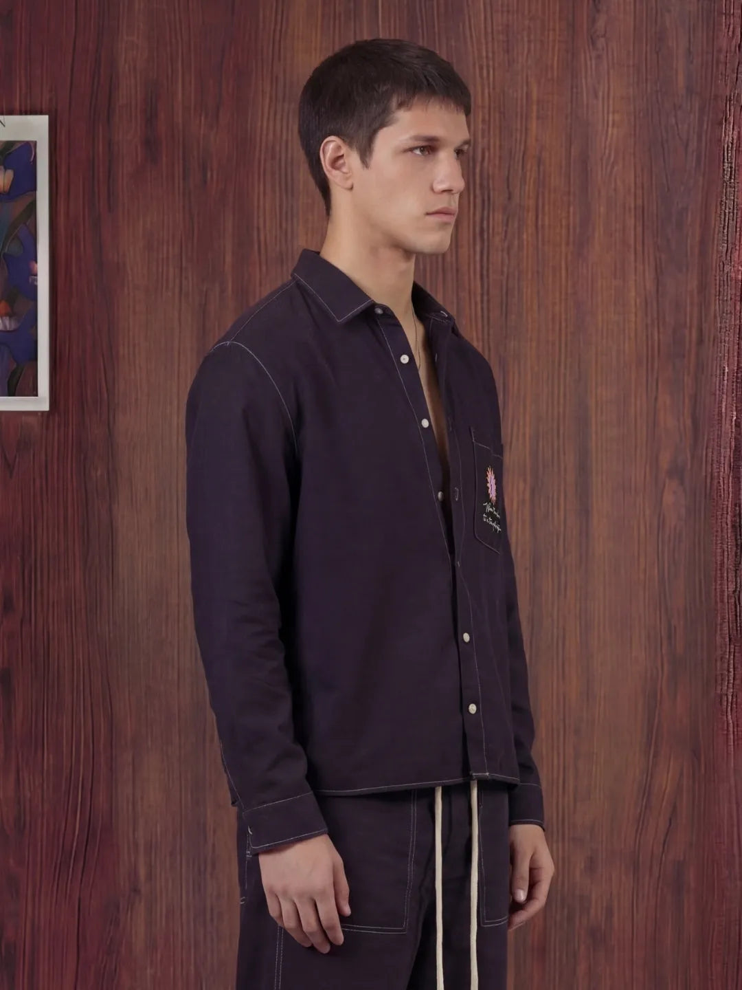 Man wearing a black shirt and pants against a wooden wall.