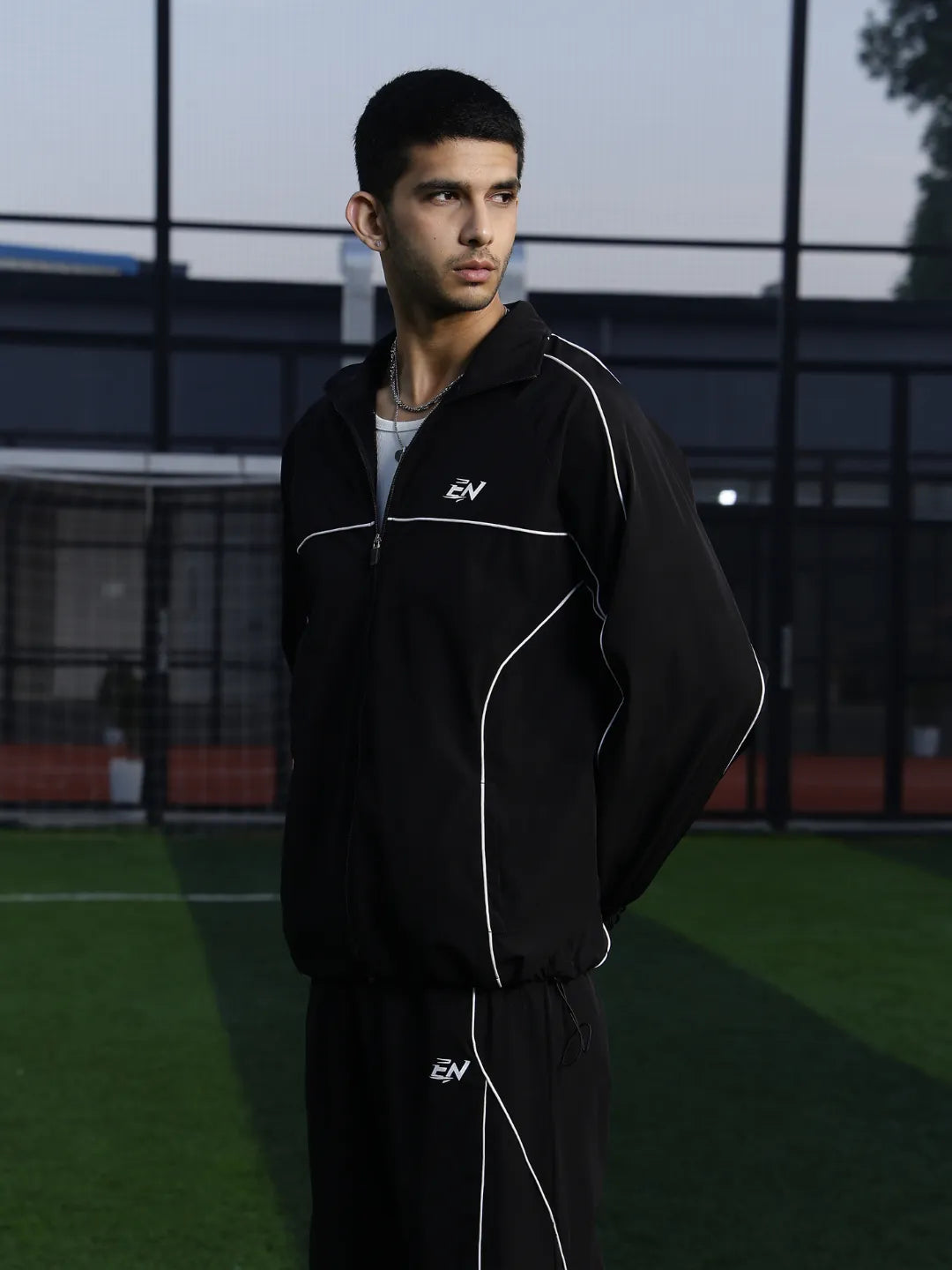 Man wearing a black sports jacket with a logo on a sports field
