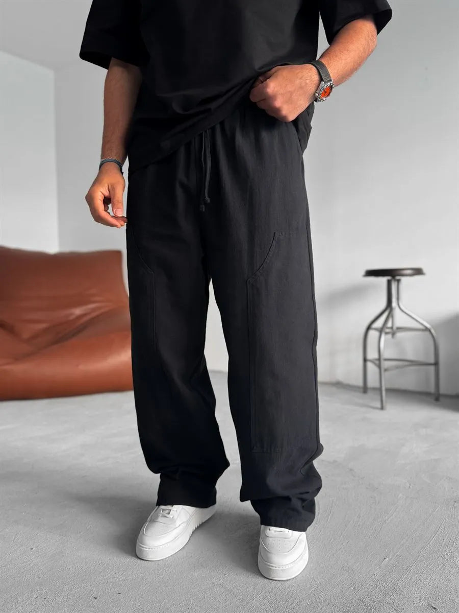 Person wearing black linen pants and white shoes in a minimalistic room with a brown bean bag and metal stool.