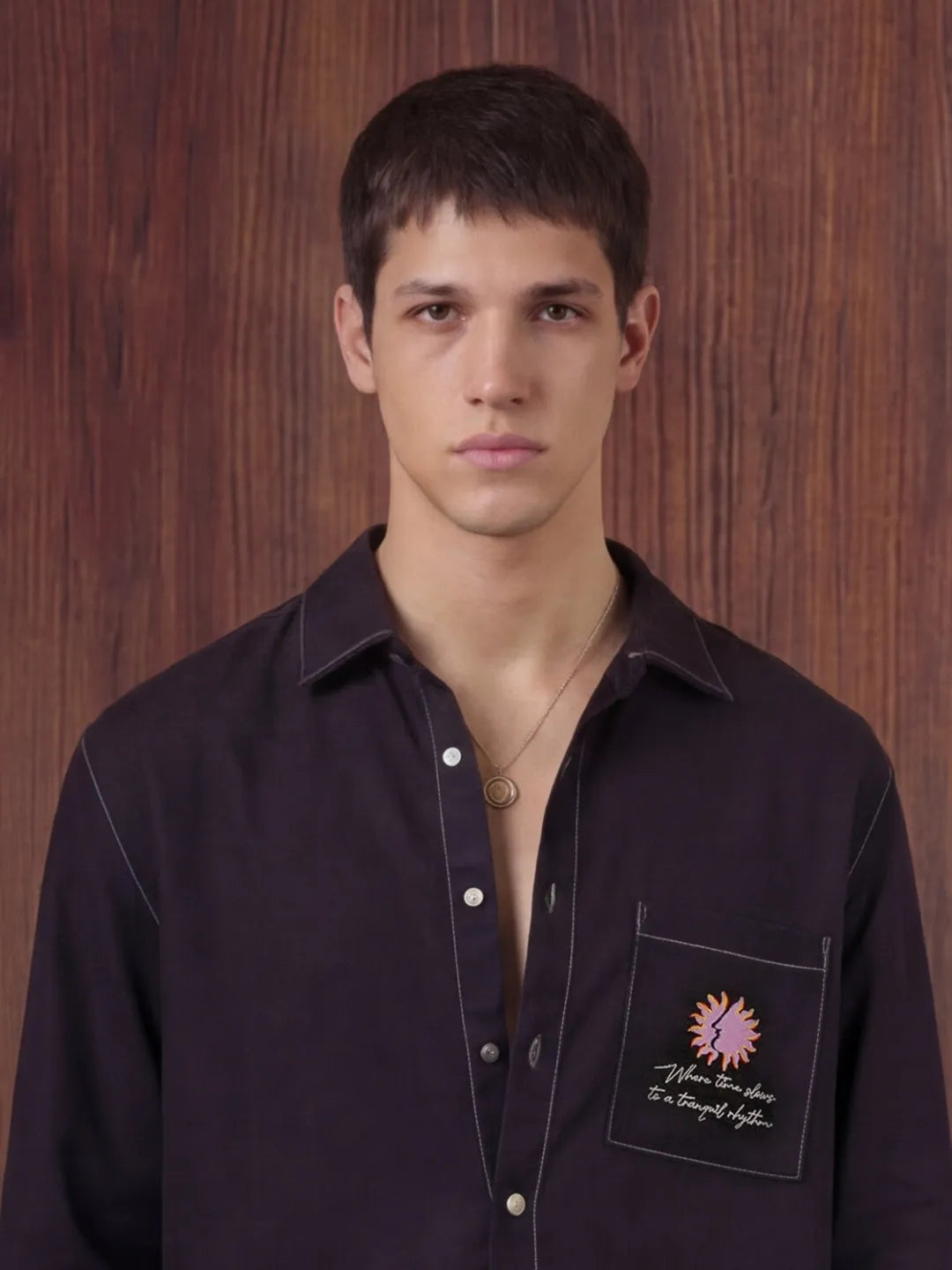 Man wearing a black shirt with a logo on a wooden background