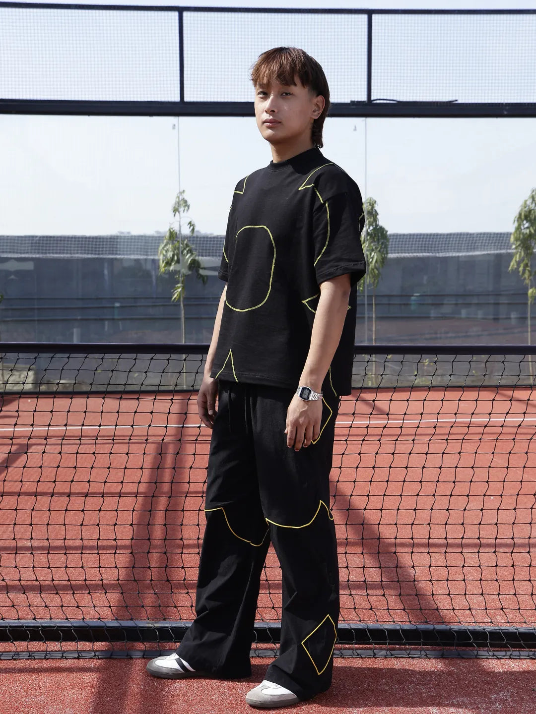 Person wearing a black outfit with yellow accents on a tennis court