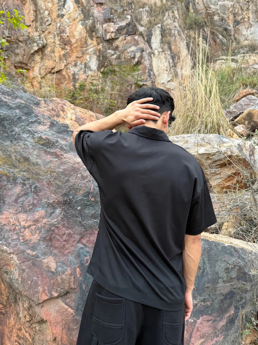 Person wearing a black shirt and pants standing in front of a rocky landscape.