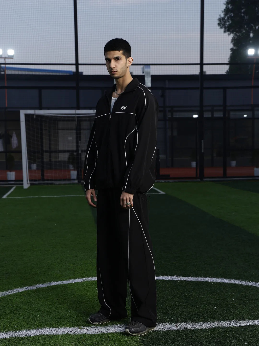Person wearing a black tracksuit on a sports field at night