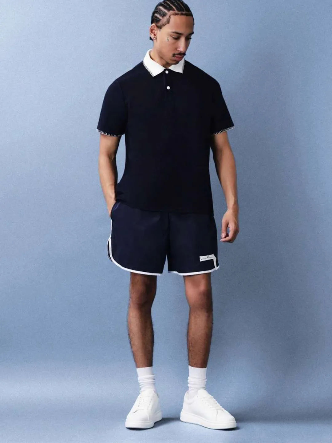 Man wearing a navy polo shirt and shorts with white accents on a light blue background