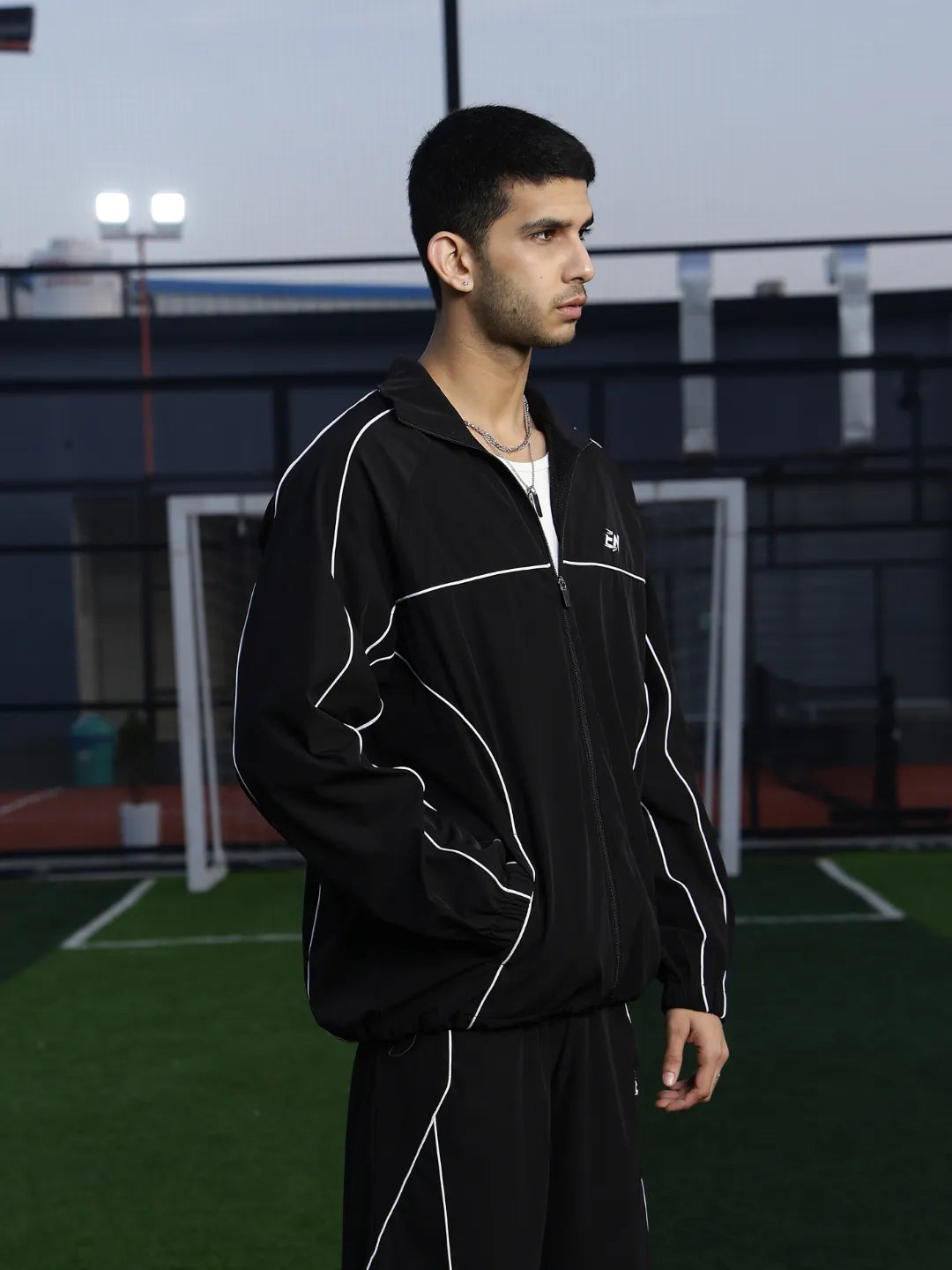 Man wearing a black sports jacket  with white accents on an outdoor sports court.