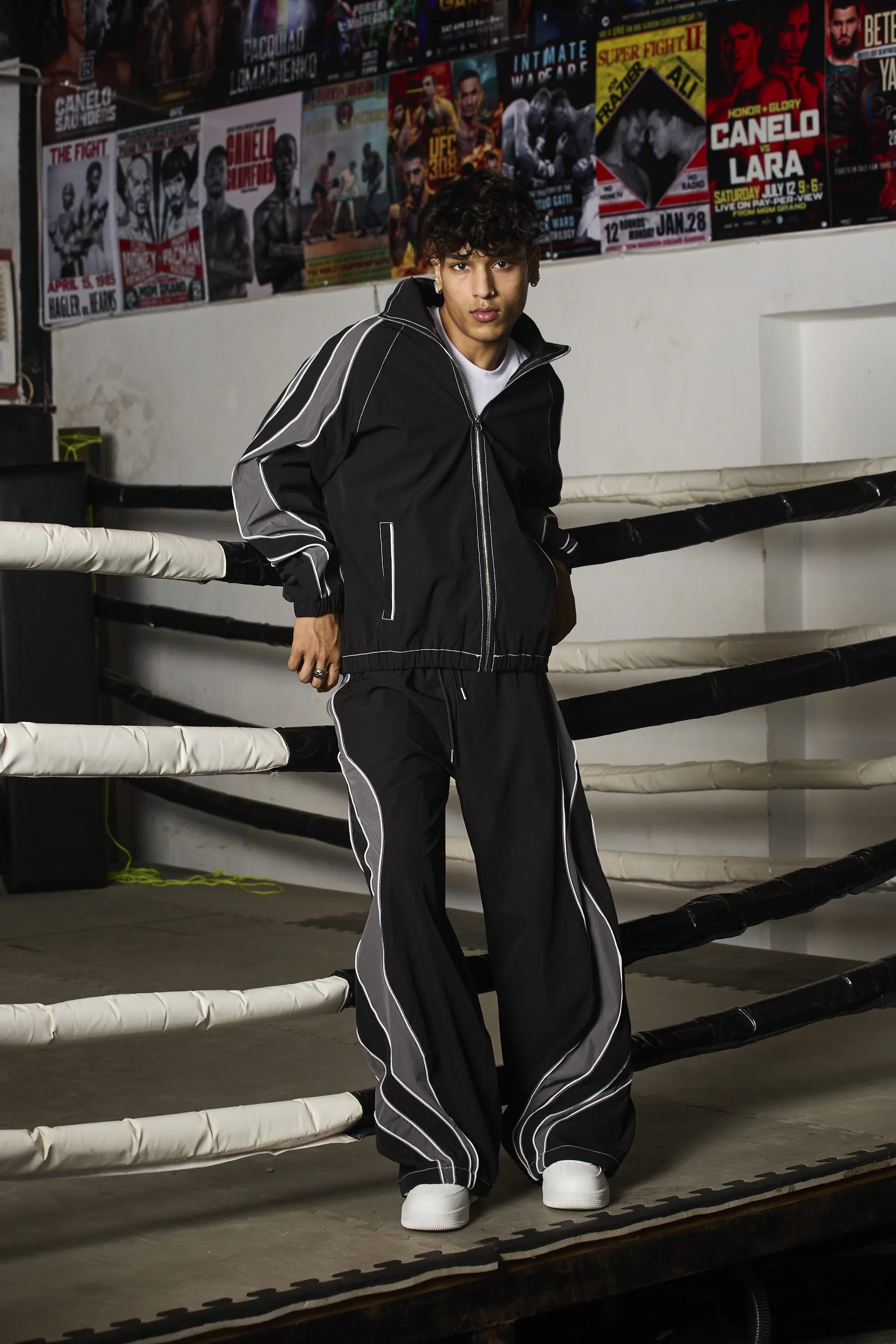 Person wearing a black tracksuit with white stripes in a boxing ring setting
