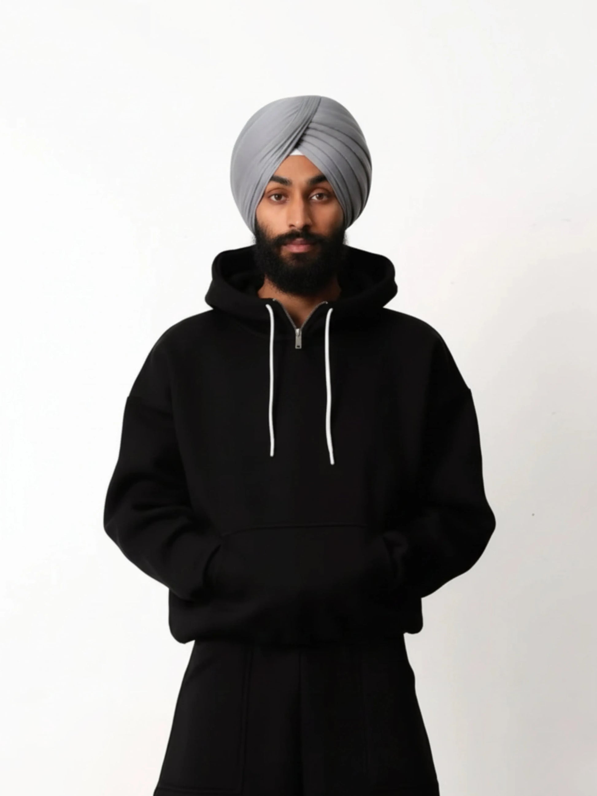 Person wearing a black hoodie and grey turban on a white background