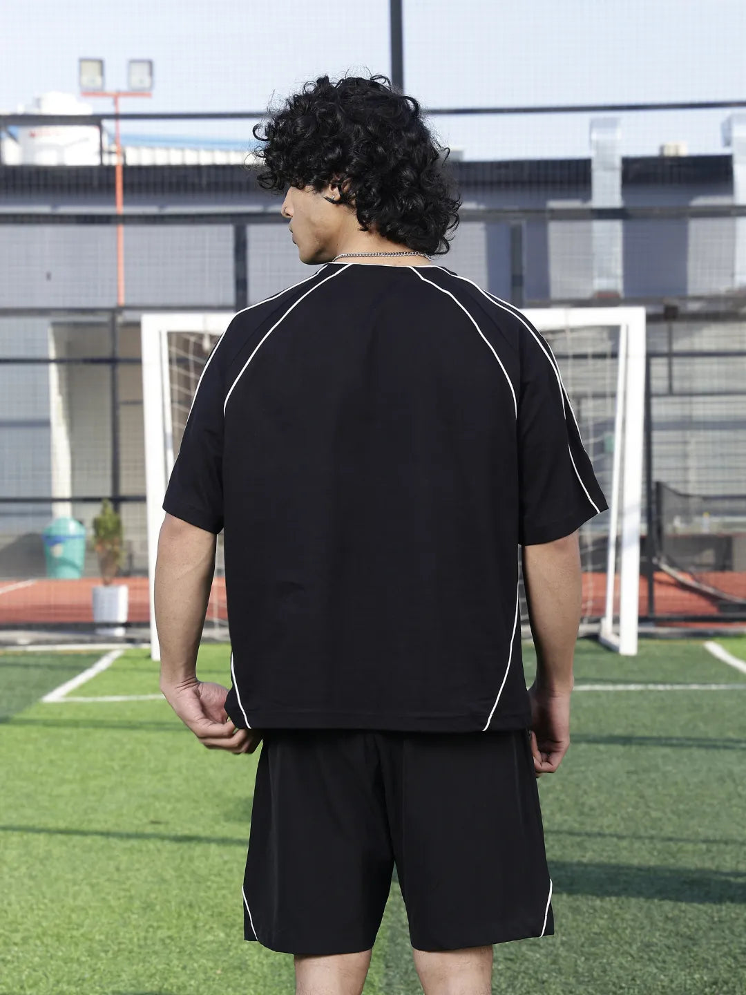 Person wearing a black sports outfit with white piping on a soccer field.