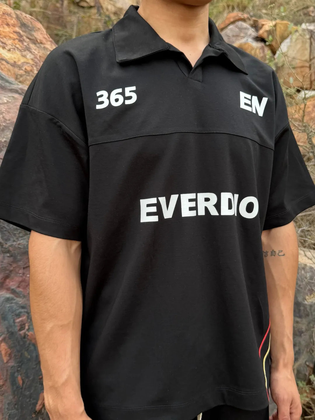 Person wearing a black shirt with '365' and 'EVERDION' branding against a rocky background
