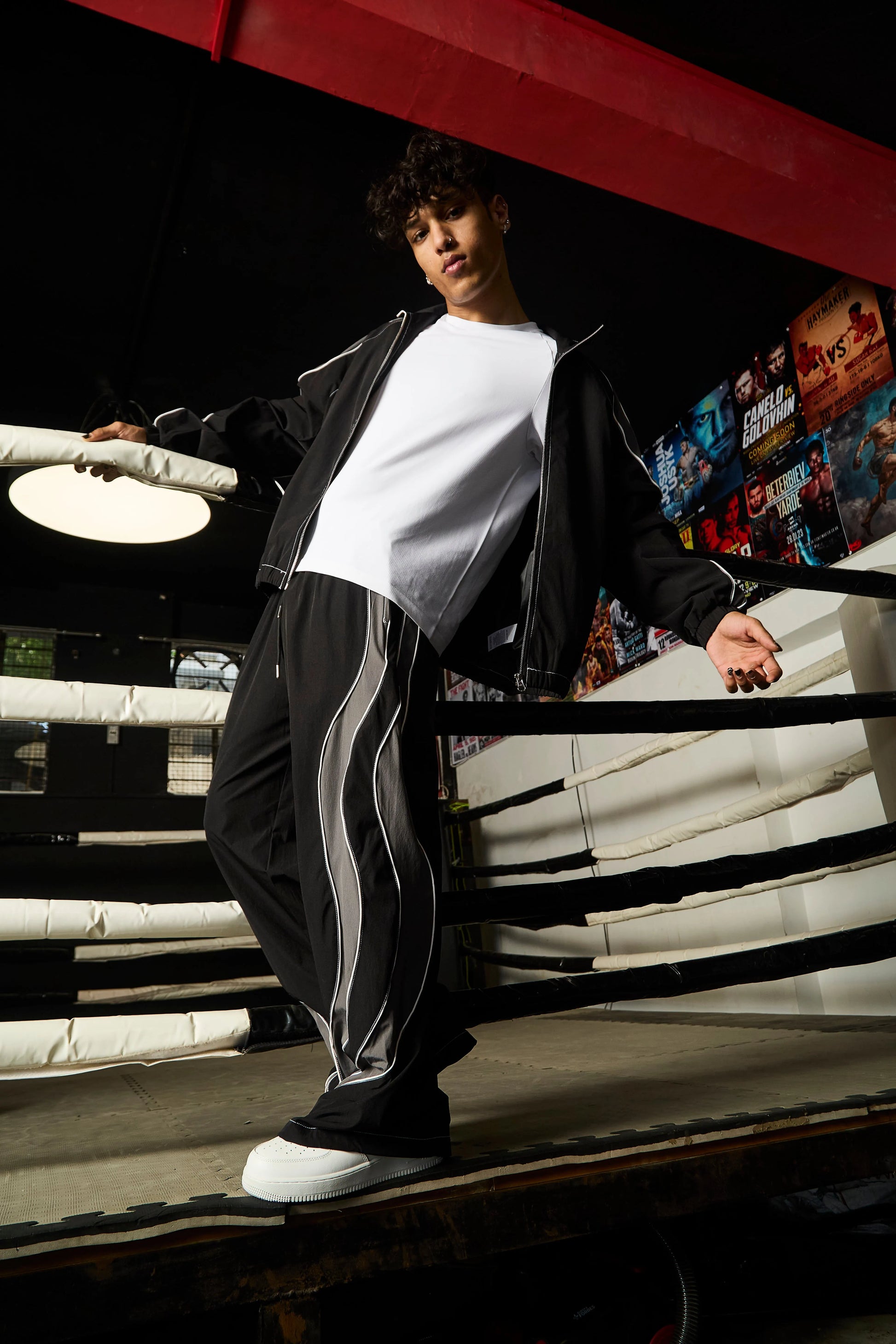 Person wearing a black tracksuit with white stripes in a boxing ring setting