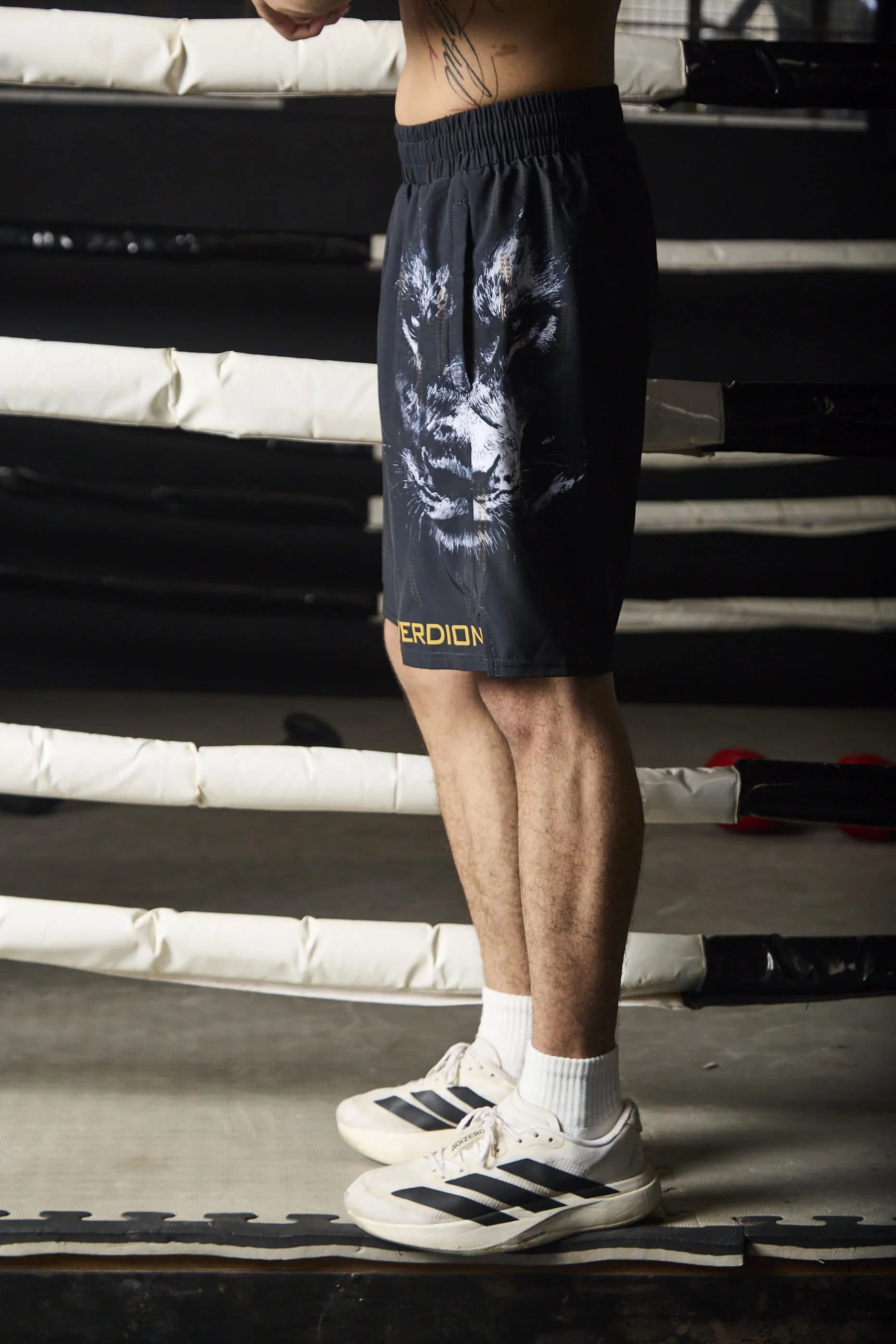 Person wearing black athletic shorts with a logo on a boxing ring.