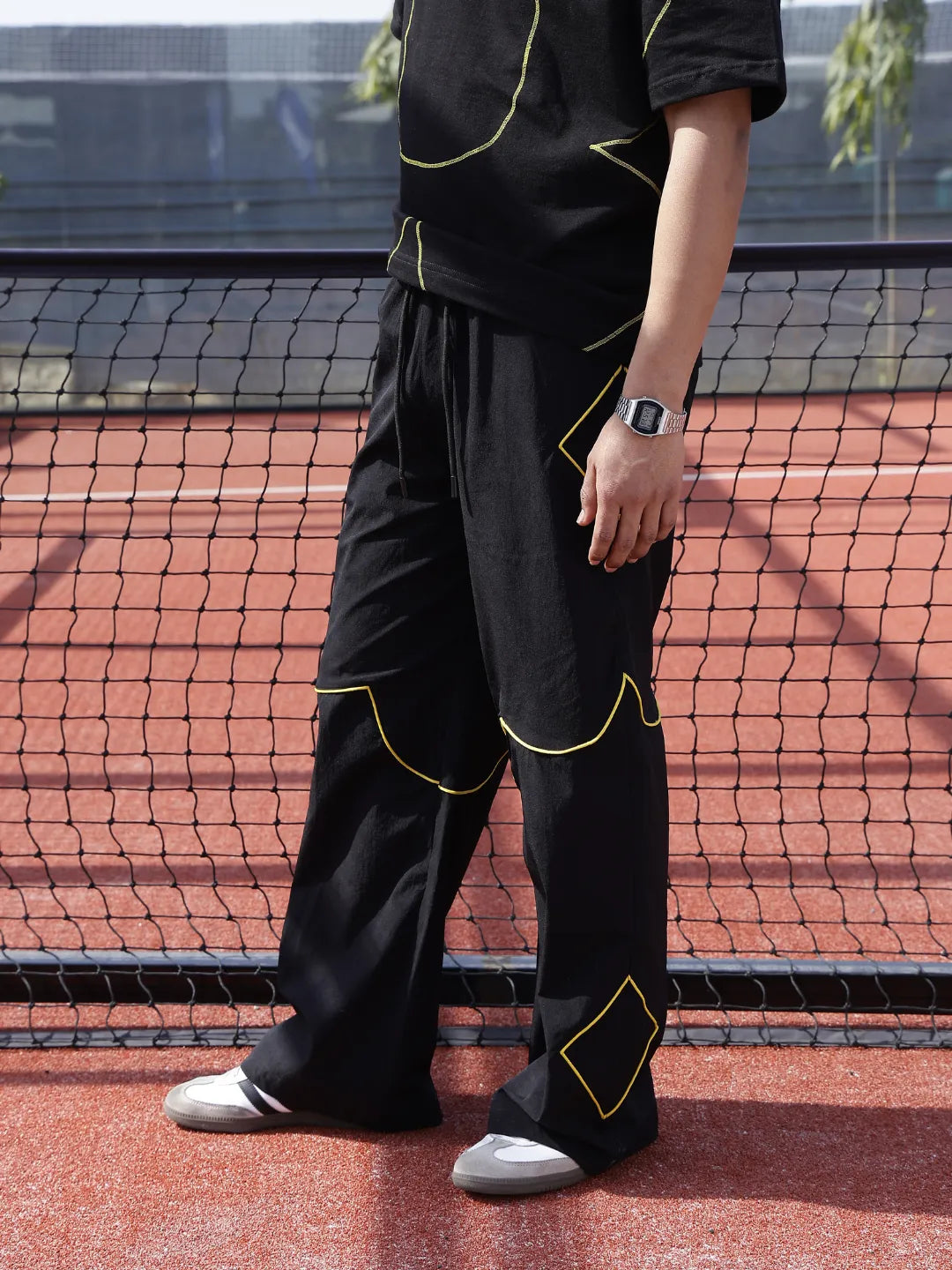 Person wearing a black outfit with yellow accents on a tennis court.