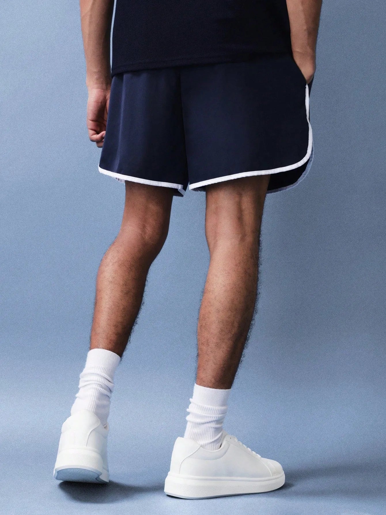 Person wearing navy shorts with white trim and white sneakers on a grey background