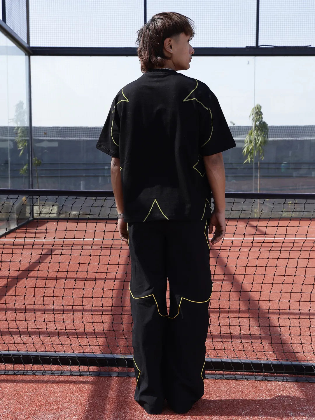 Person wearing a black outfit with yellow accents on a tennis court.