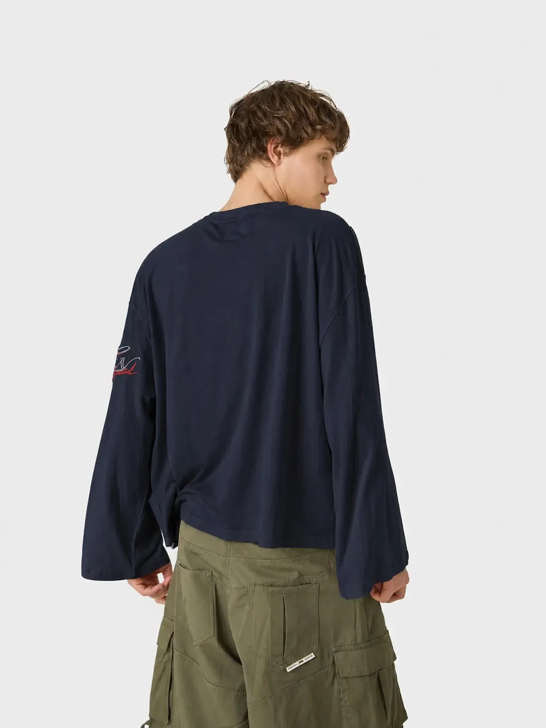 Person wearing a navy long-sleeve oversized t-shirt with a patch on the back, standing against a white background