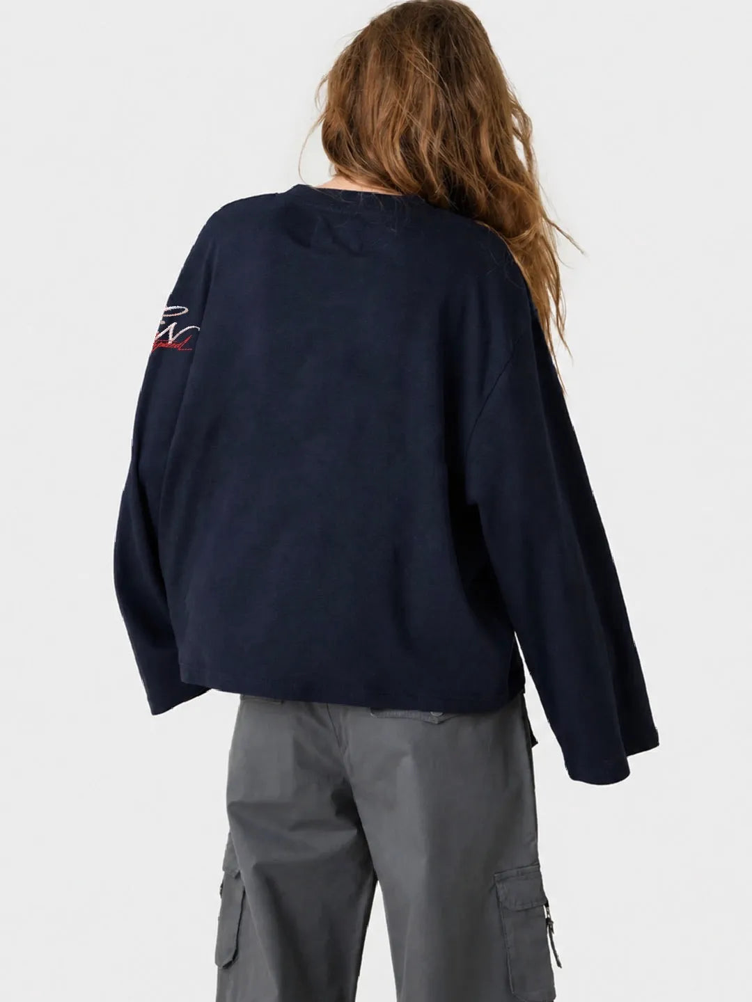 Person wearing a navy blue long sleeve oversized t-shirt with a logo on the sleeve against a white background