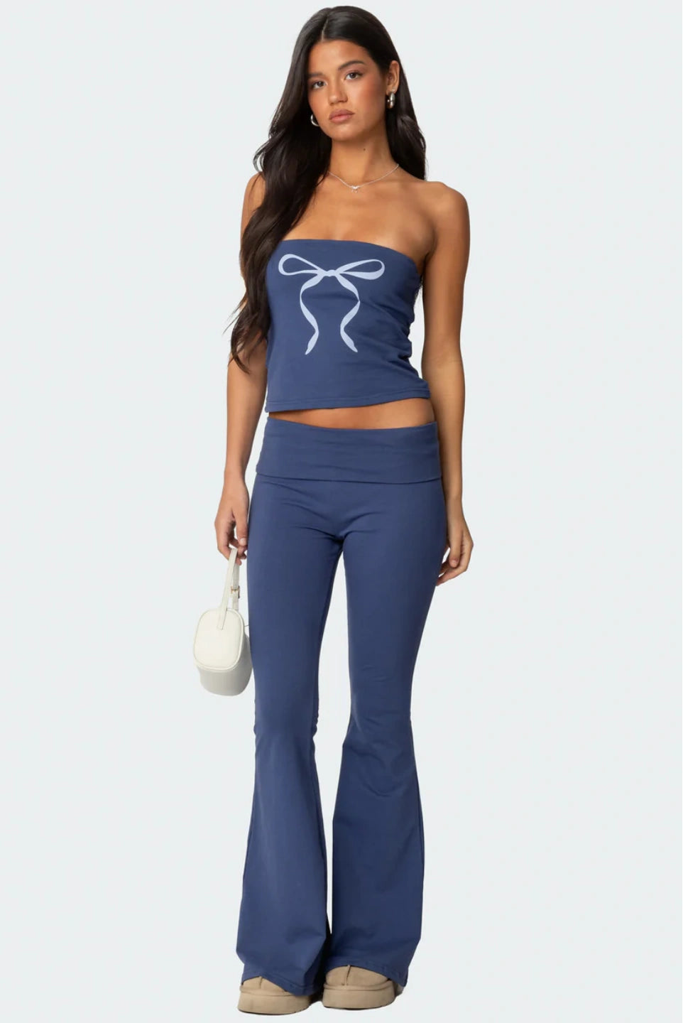 Woman wearing a blue strapless top and flared pants with a white bow design on a white background