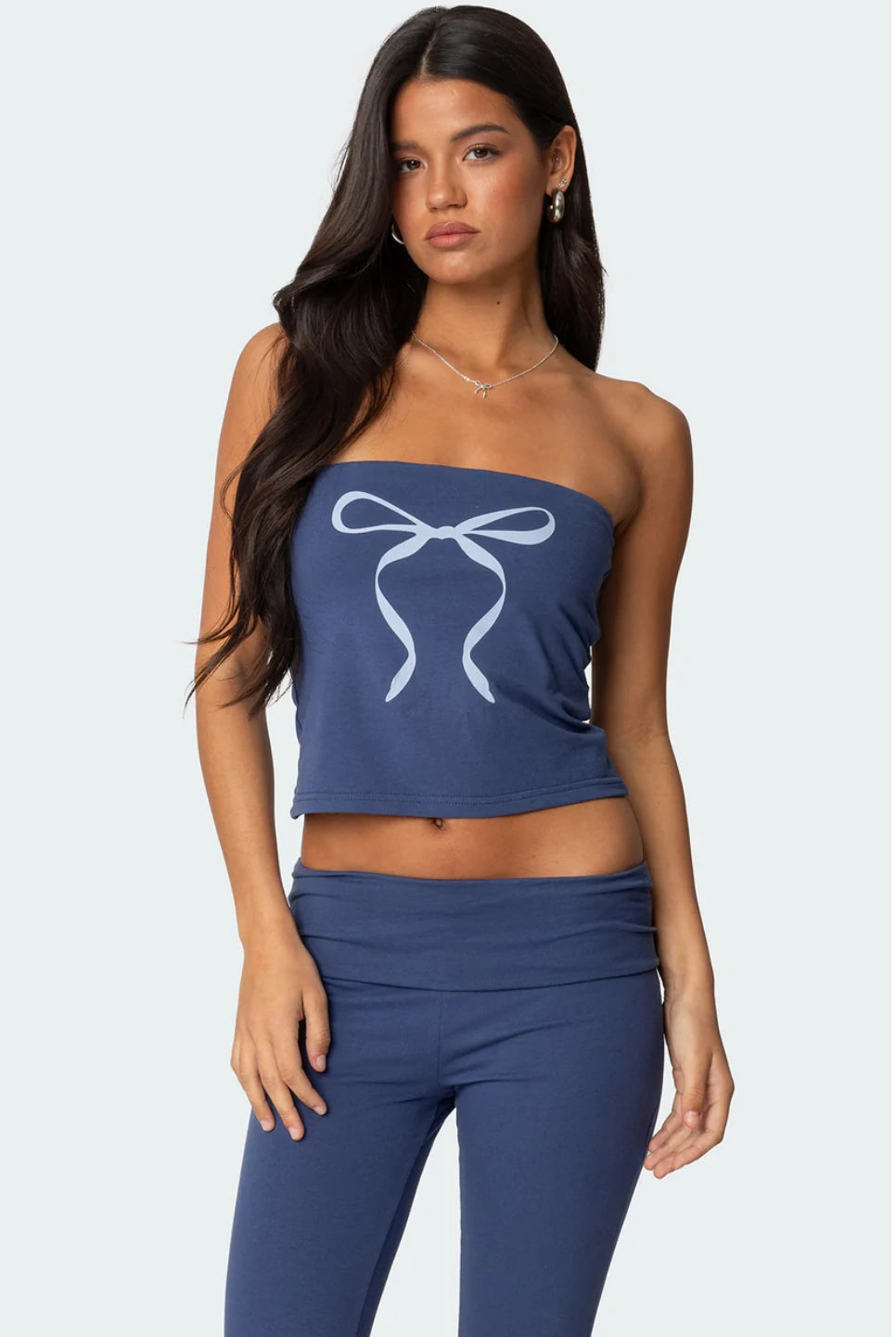 Woman wearing a blue strapless top with a bow design and matching pants on a white background