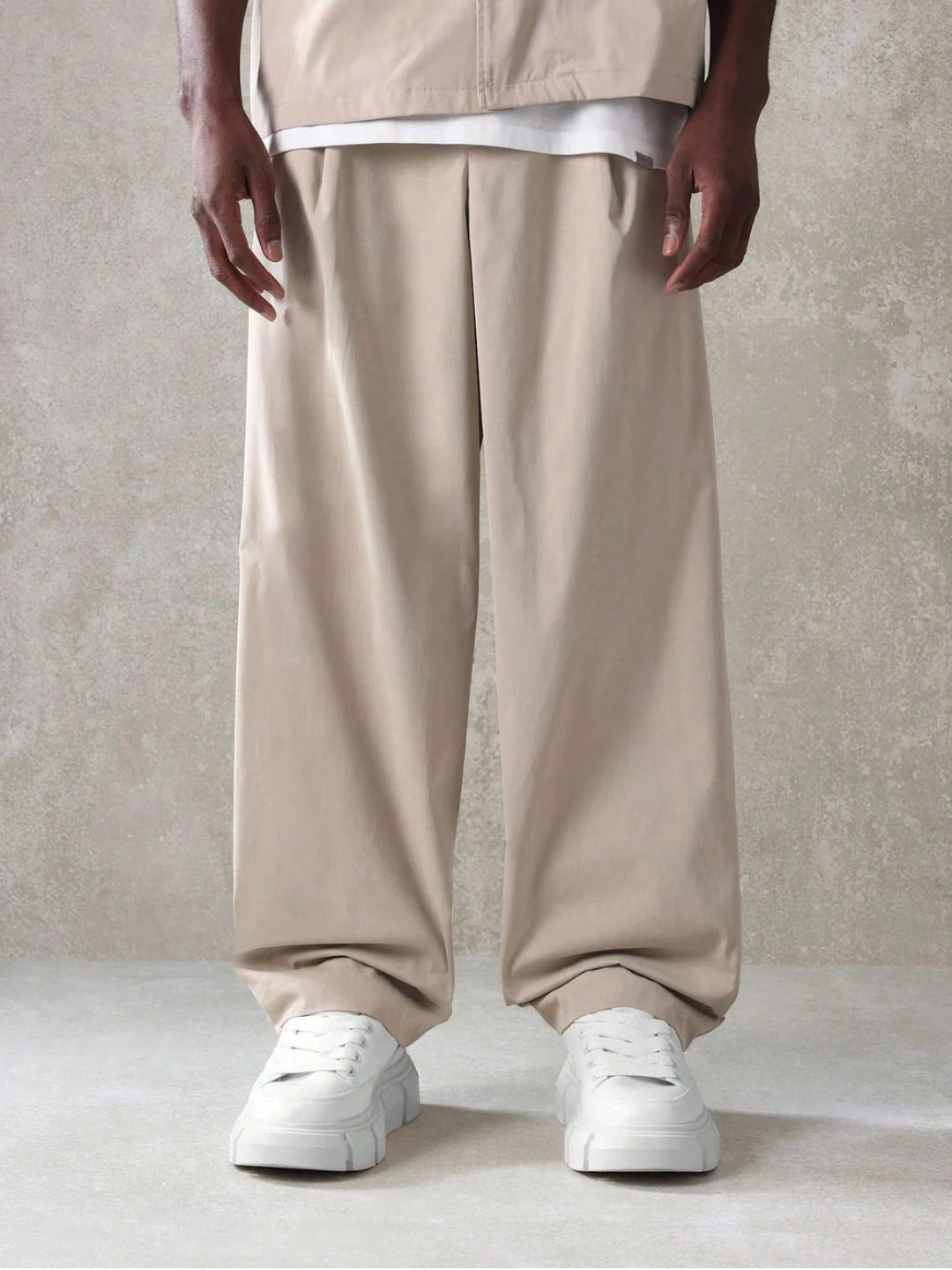 Person wearing beige wide-leg pants and white sneakers on a neutral background