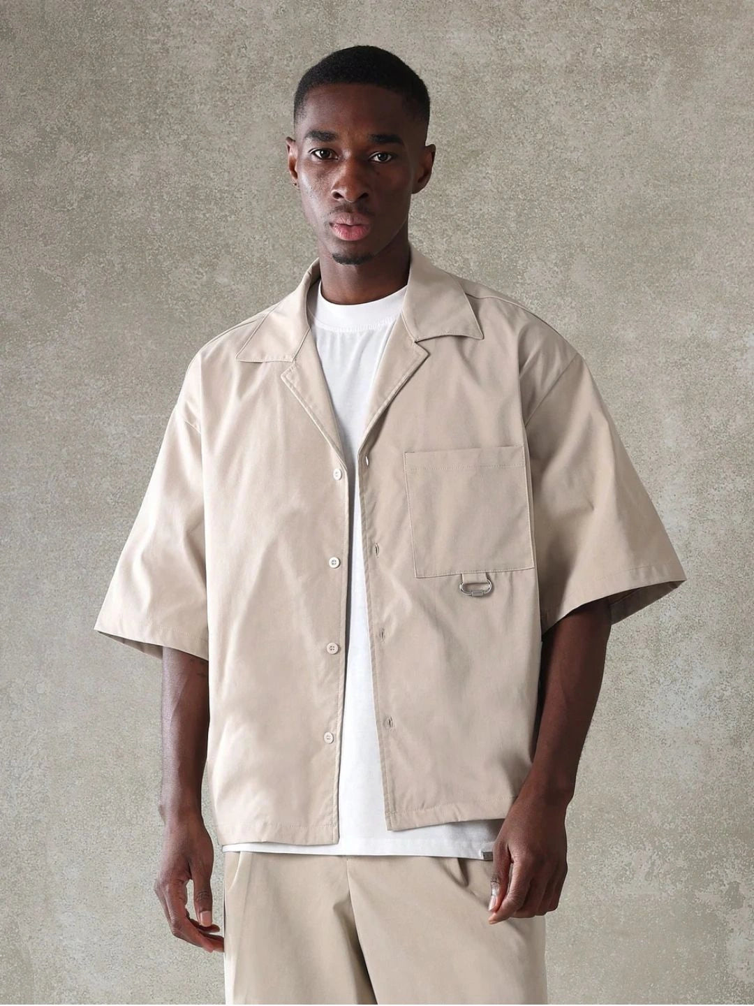Man wearing a beige short-sleeve shirt over a white tshirt against a grey background