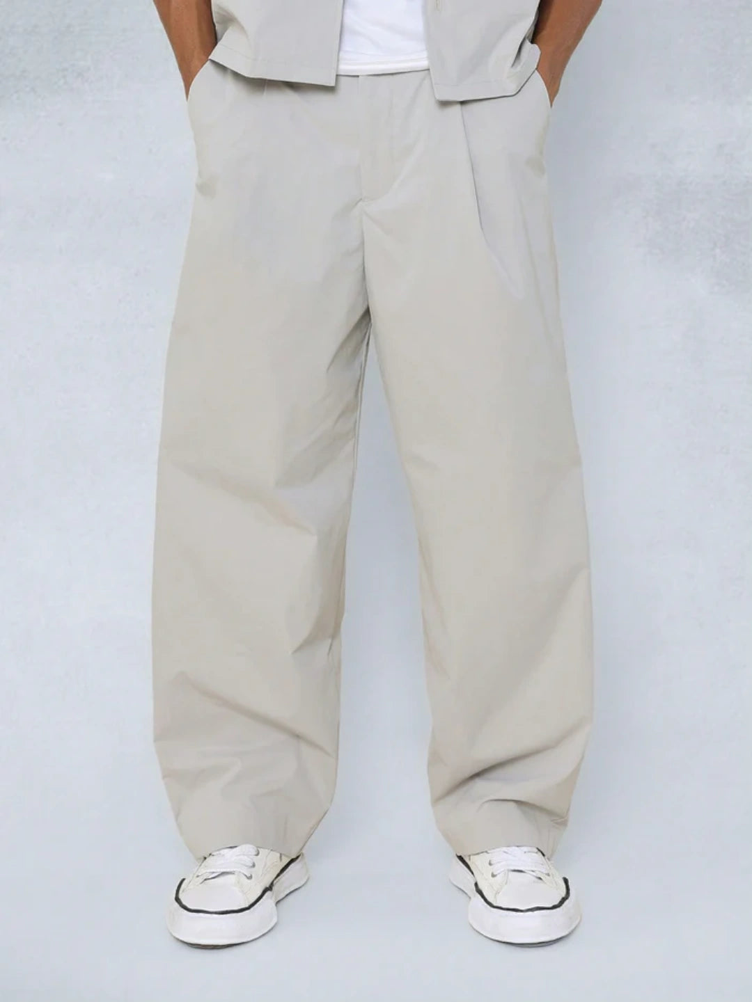 Person wearing beige wide-leg pants and white sneakers on a light grey background