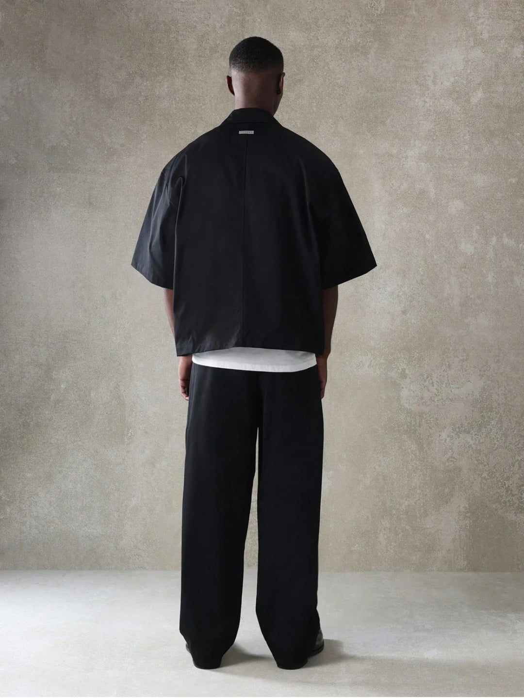 Person wearing a black outfit against a beige wall