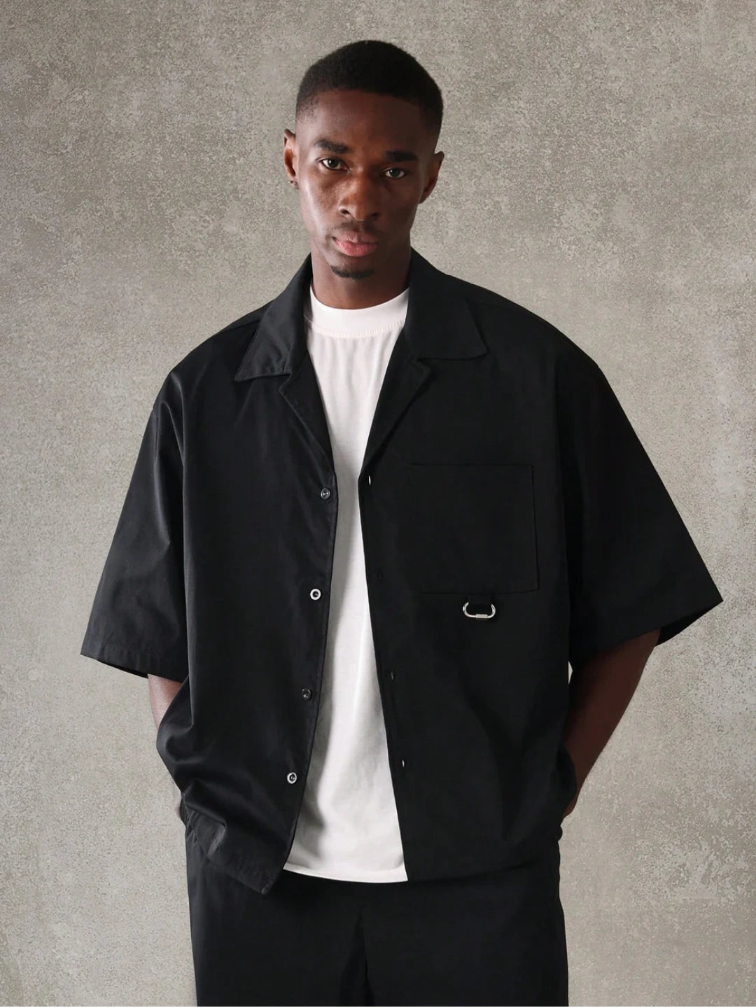 Man wearing a black jacket over a white shirt against a grey background