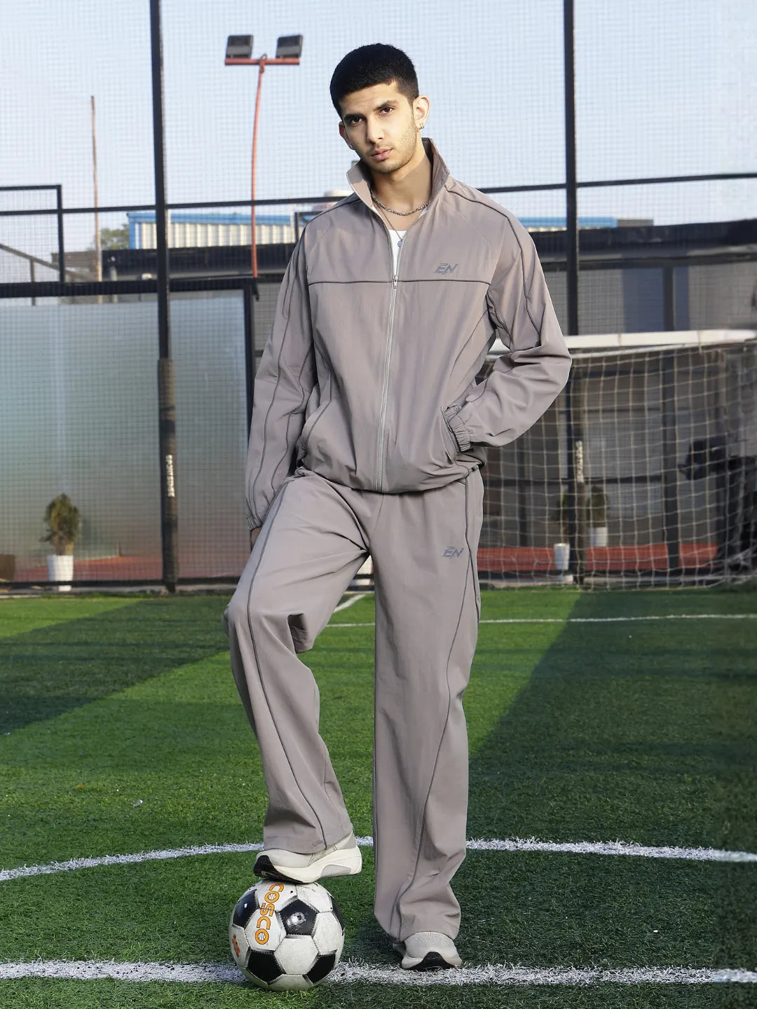 Person wearing a grey tracksuit standing on a soccer field with a soccer ball.