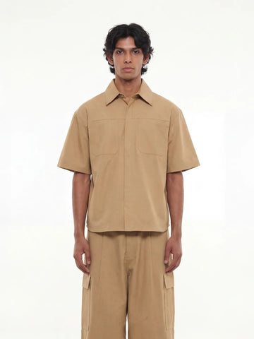 Man wearing a beige short-sleeve shirt and pants on a white background