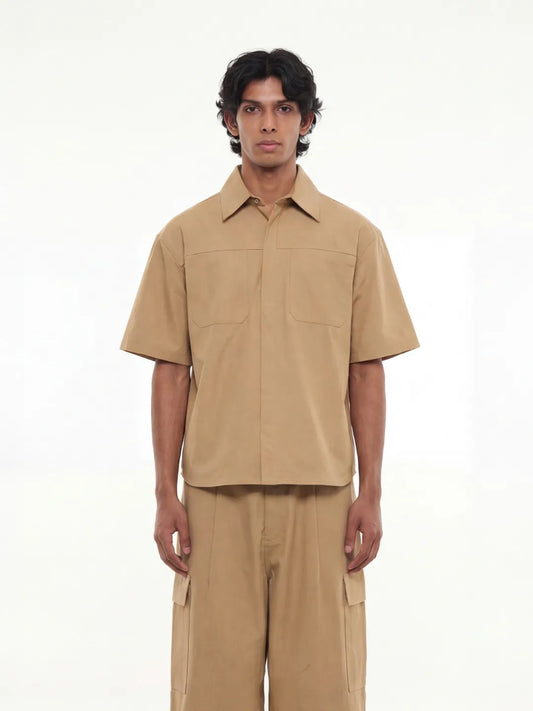 Man wearing a beige short-sleeve shirt and pants on a white background