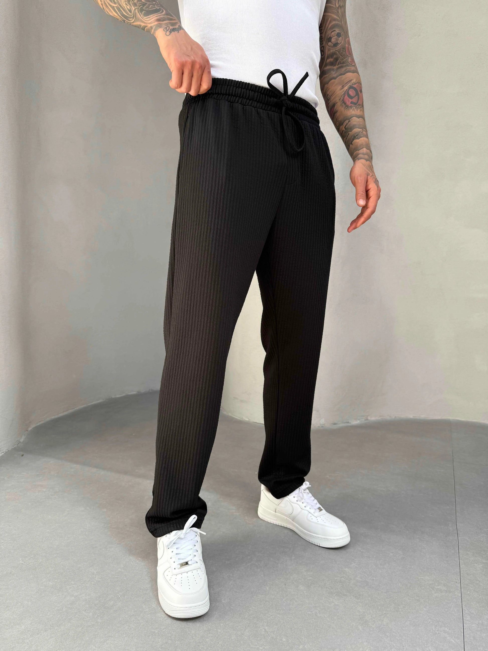Person wearing black ribbed jogger and white sneakers on a plain background