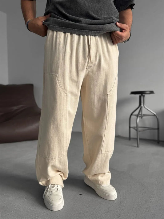 Person wearing beige linen pants and white sneakers in a minimal indoor setting