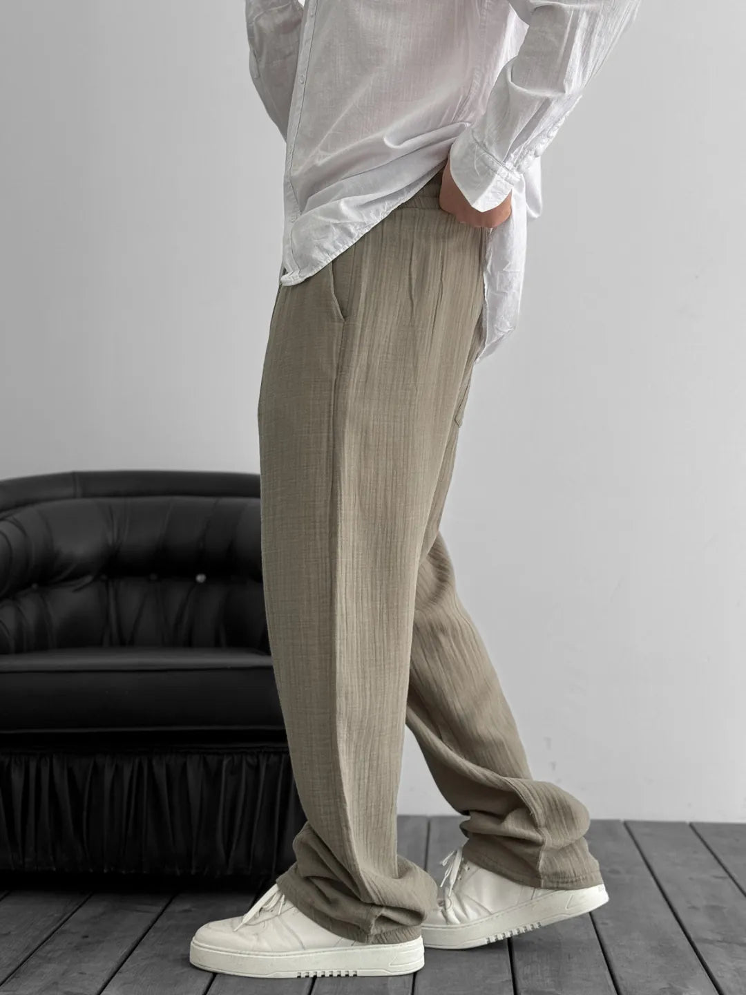 Person wearing beige pants and a white shirt in a minimalistic setting with a black couch.