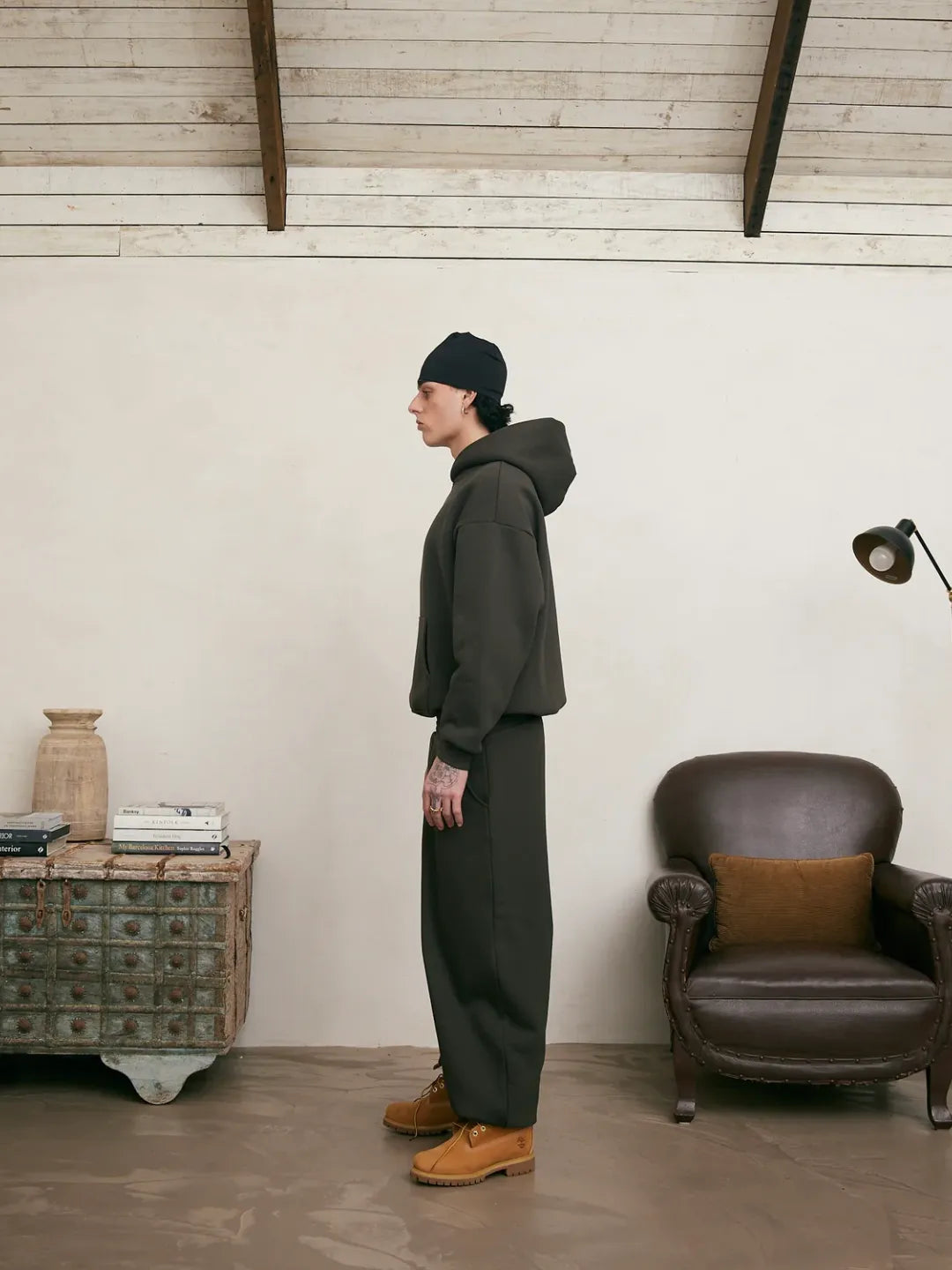 Person wearing a dark outfit standing in a room with a wooden floor and white walls.