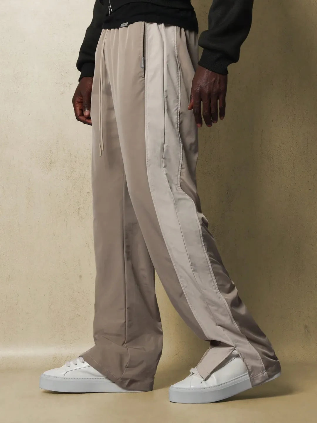 Person wearing beige track pants with white stripes on a beige background