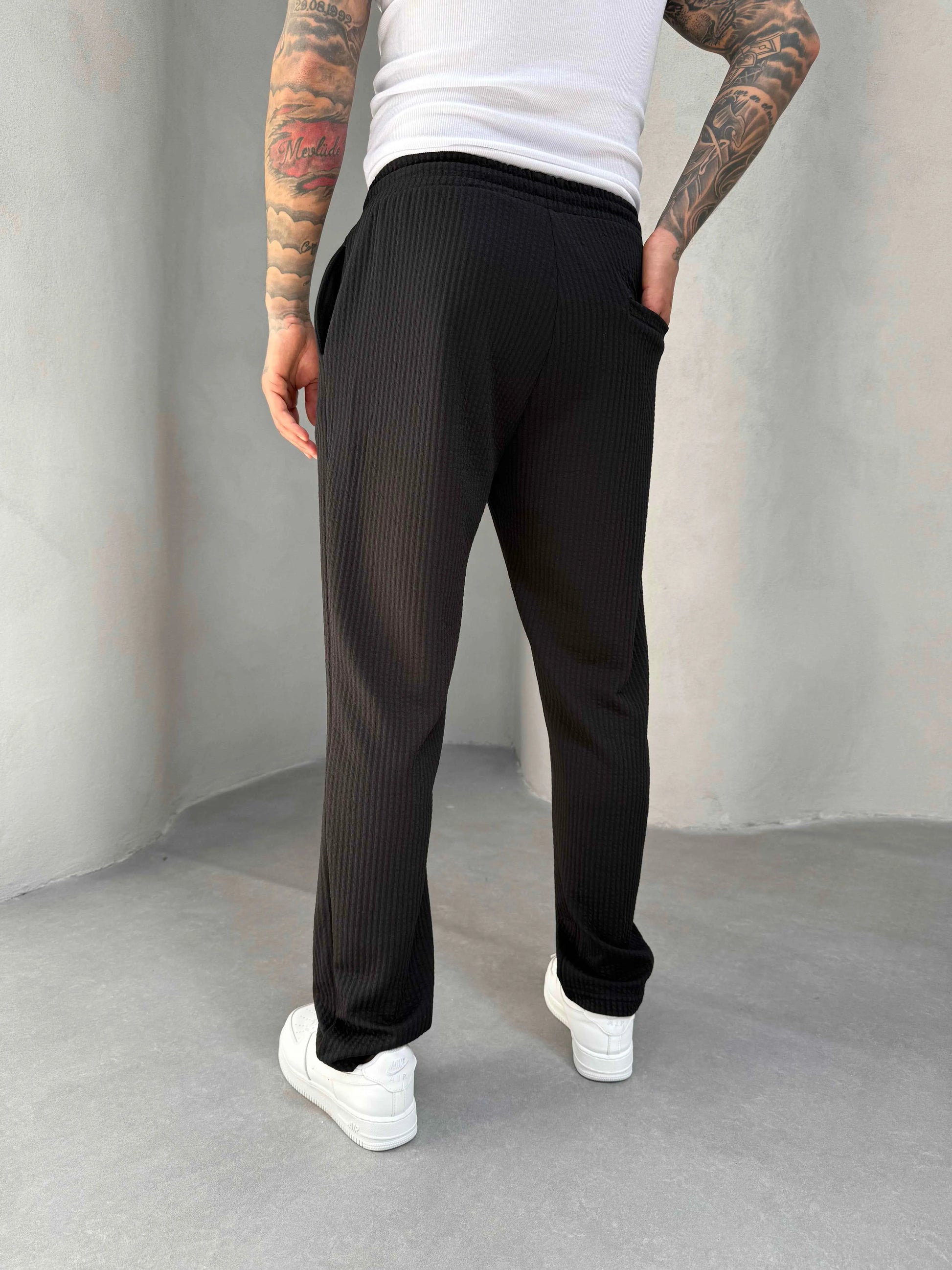 Person wearing black ribbed jogger and white sneakers on a plain background