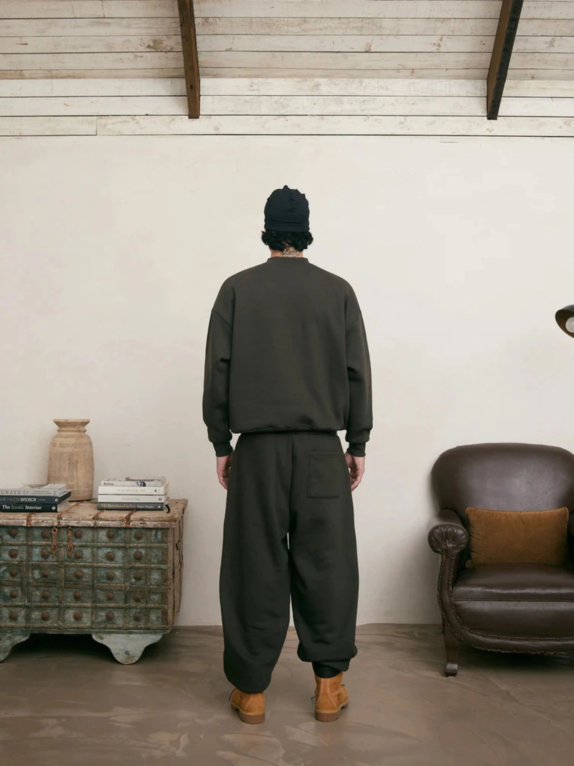 Person wearing a coffee sweatshirt and sweatpants set standing in a room with a wooden cabinet and leather chair.