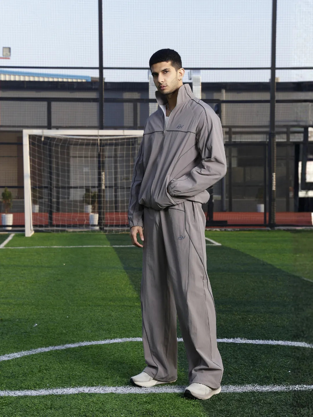 Person wearing a grey tracksuit on a sports field with a goalpost in the background.